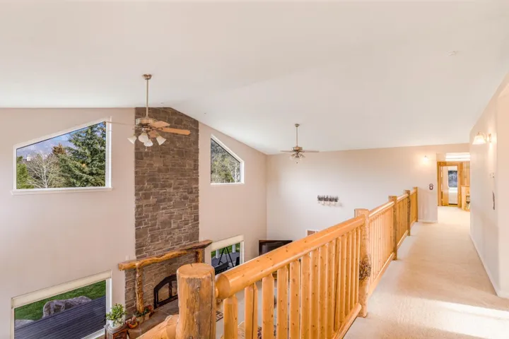 Expansive great room featuring a floor-to-ceiling stone fireplace with a log mantel, vaulted ceilings, and a wood-finish railing