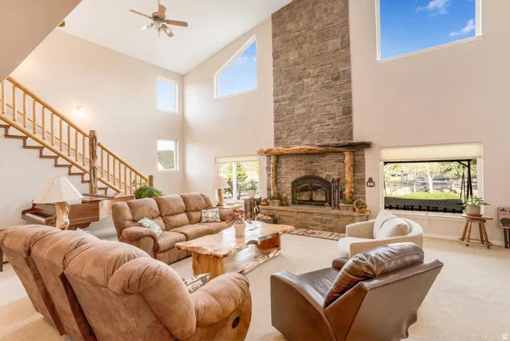 Two-story living area featuring a stone fireplace with a rustic wood mantel, a multi-level staircase with wood railings, and multiple high windows