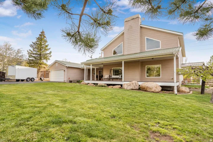 Expansive green lawn with a two-story residence featuring a covered porch, multiple windows, and natural stone landscaping elements