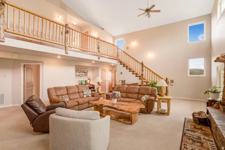 Expansive living area with a vaulted ceiling, wood-finish staircase and upper railing, recessed lighting, and high-set windows