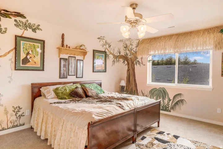 Hardwood bed frame with footboard, ceiling fan with integrated lighting, wall-mounted shelving, and a large window with white trim