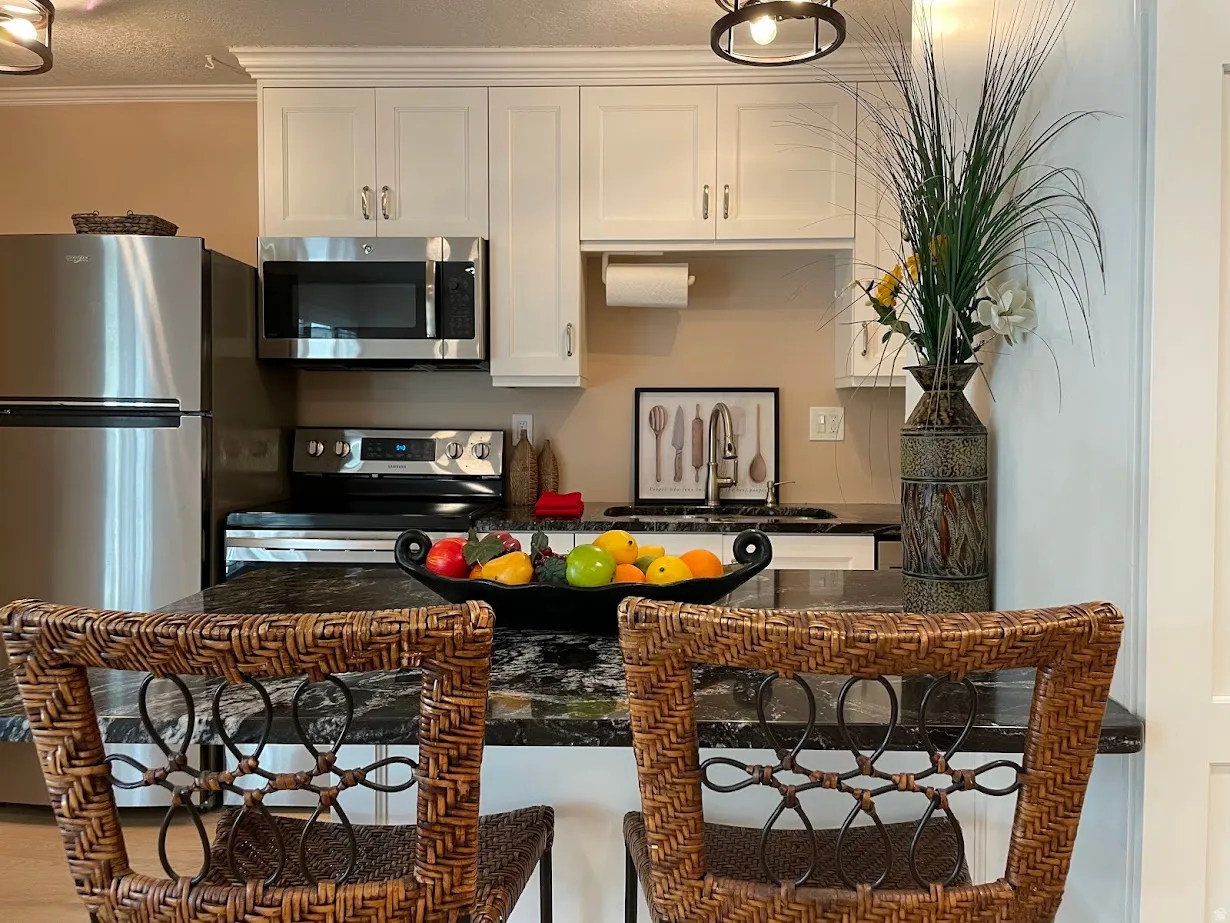 Kitchen featuring white cabinetry, stainless steel appliances, dark granite countertops, and a kitchen island with seating