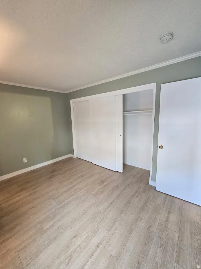 Room featuring wood-finish flooring, light green walls, white baseboards, and white crown molding