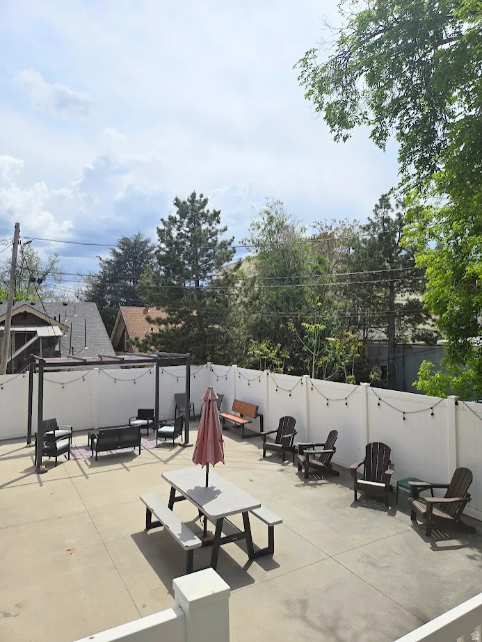 Paved patio space featuring a white privacy fence, string lighting, and a dark-toned pergola