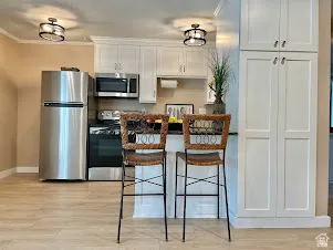 Kitchen featuring white shaker-style cabinetry, stainless steel appliances, a black countertop, and wood-finish flooring