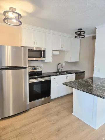 Kitchen featuring white cabinetry, stainless steel appliances, dark granite countertops, and wood-finish flooring