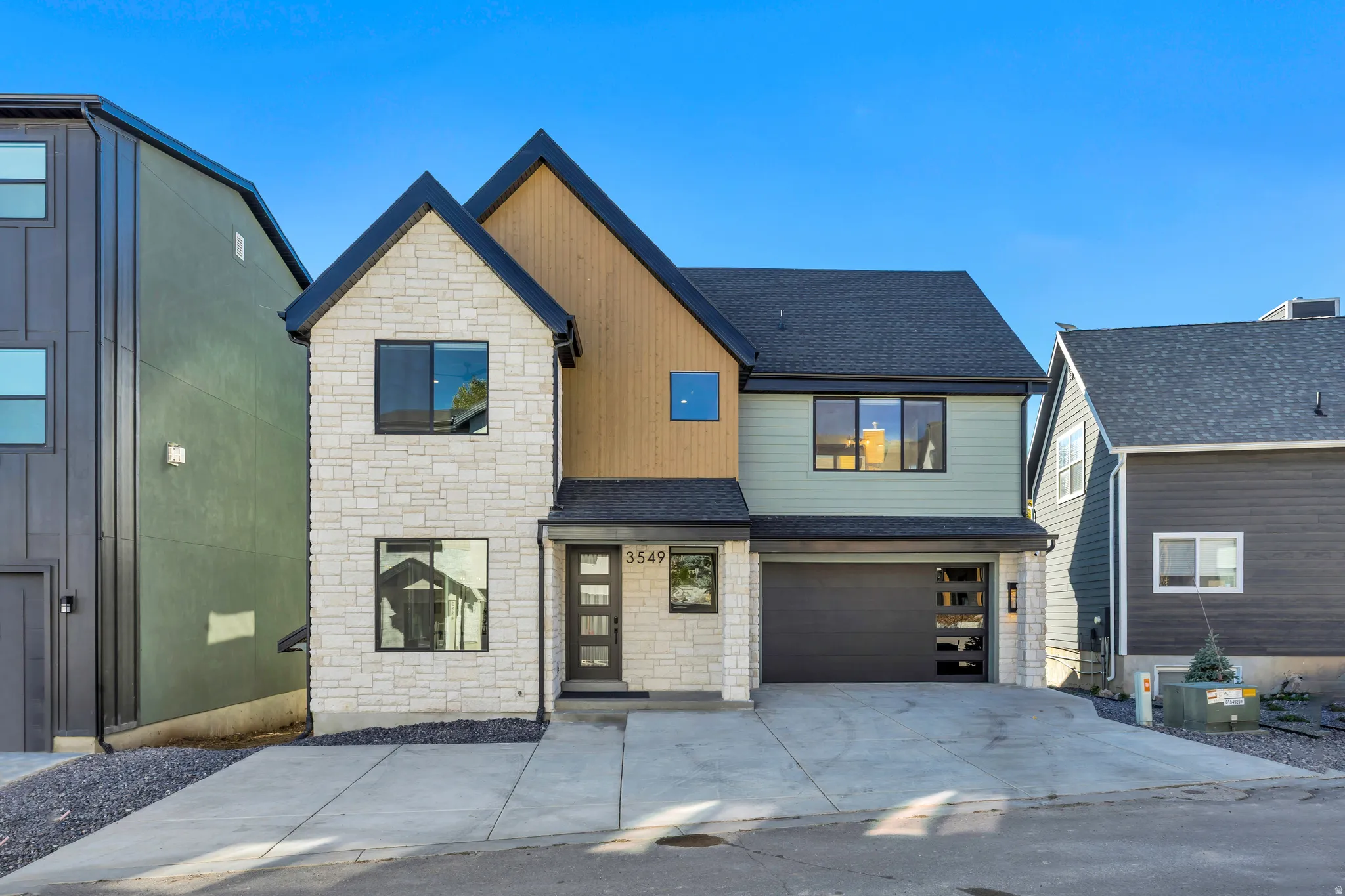 View of front of property with stone siding, an attached garage, a shingled roof, and driveway