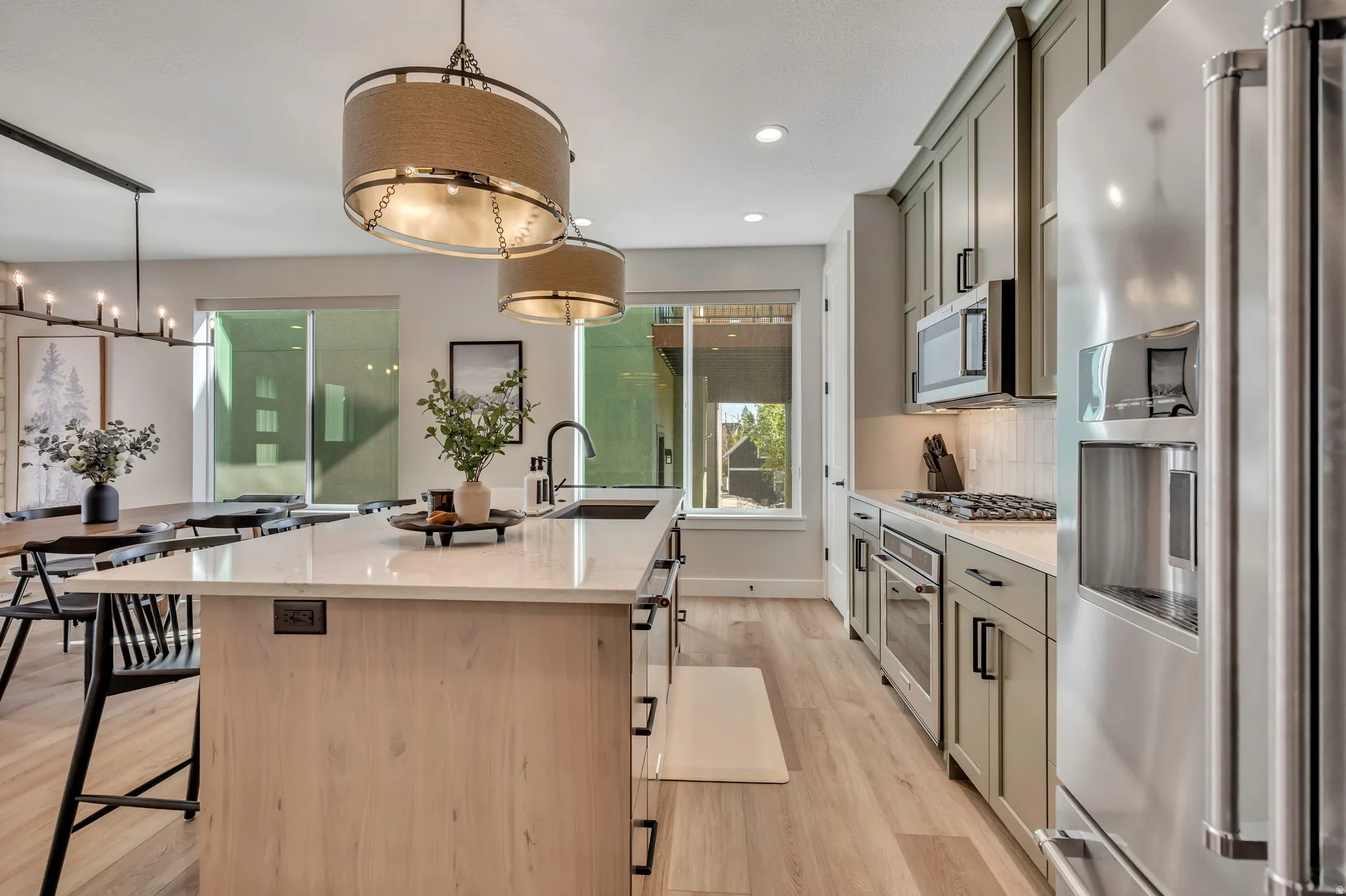 Kitchen with stainless steel appliances, a center island with sink, a kitchen bar, light stone counters, and light wood-style floors