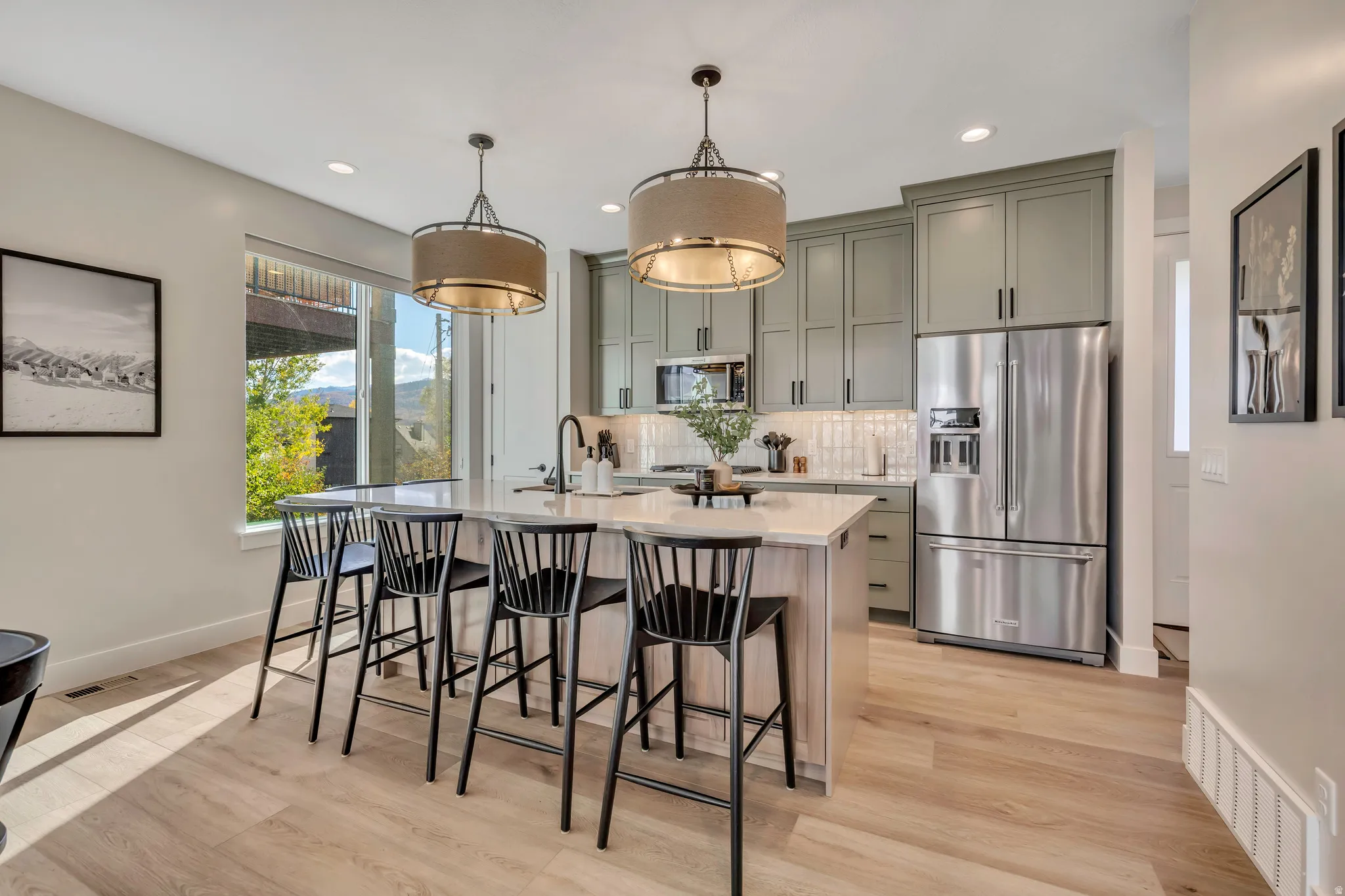 Kitchen with stainless steel appliances, a center island with sink, light stone counters, light wood-style floors, and a breakfast bar