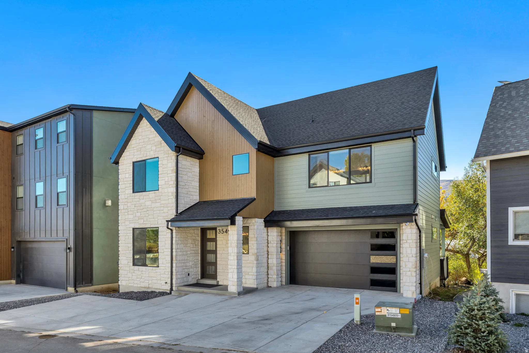 View of front of house with stone siding, an attached garage, a shingled roof, and concrete driveway