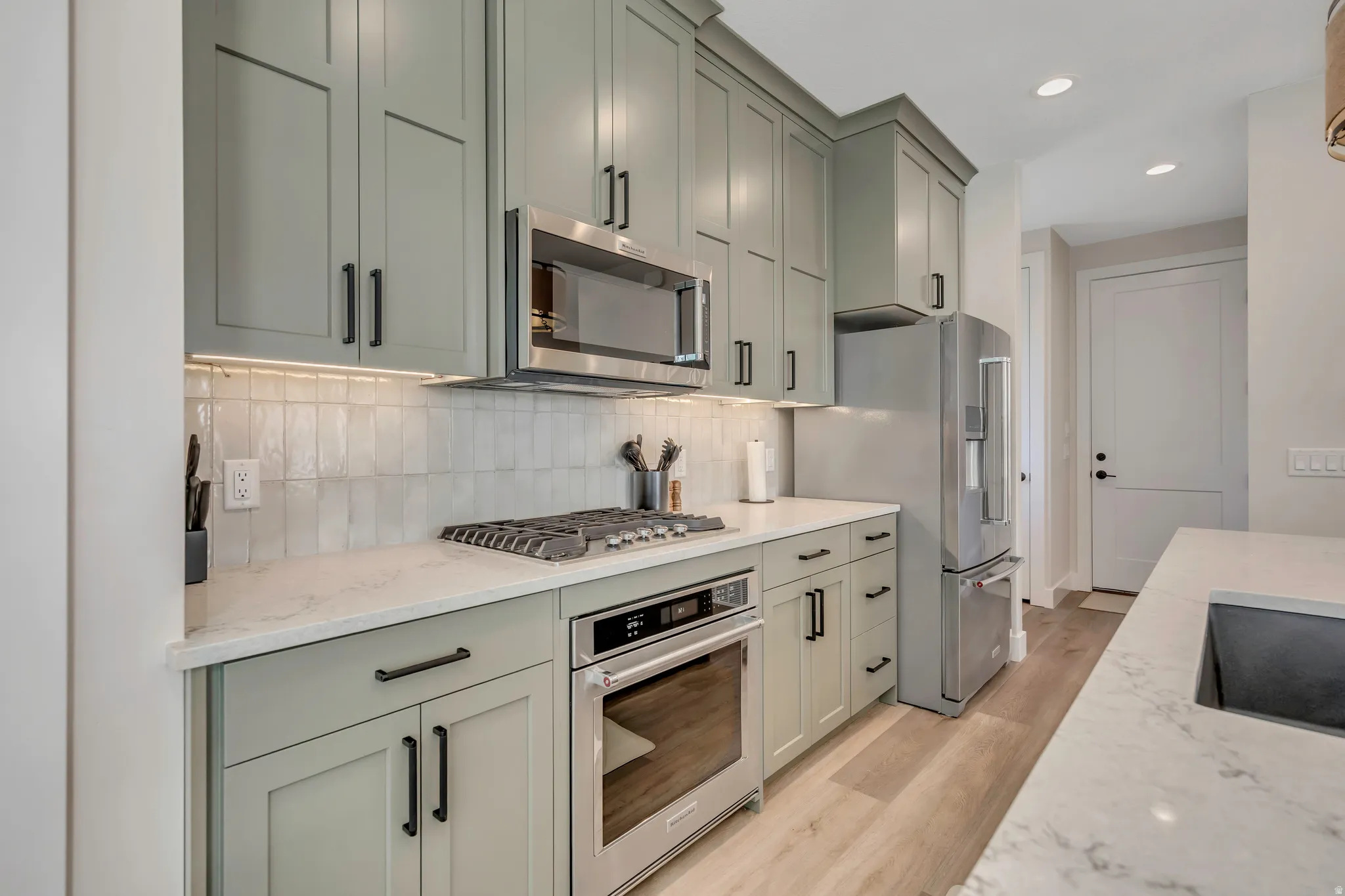 Kitchen with stainless steel appliances, light wood-style flooring, light stone countertops, backsplash, and recessed lighting