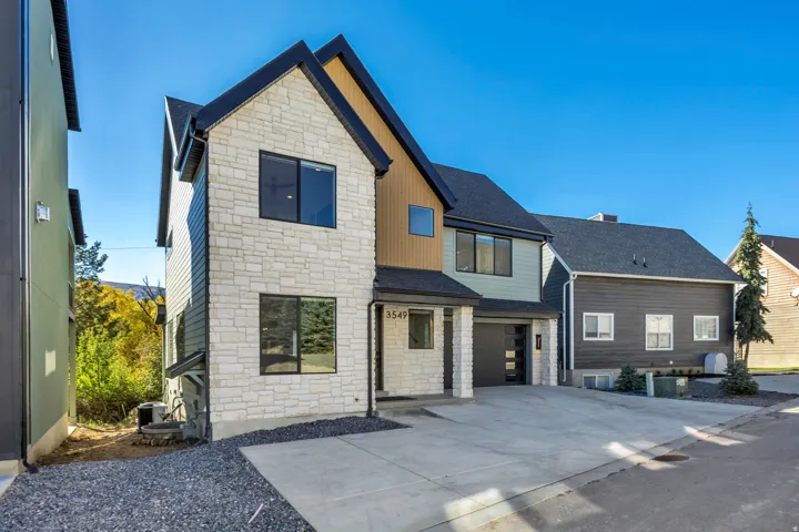 View of front of home featuring stone siding, board and batten siding, driveway, a shingled roof, and a garage