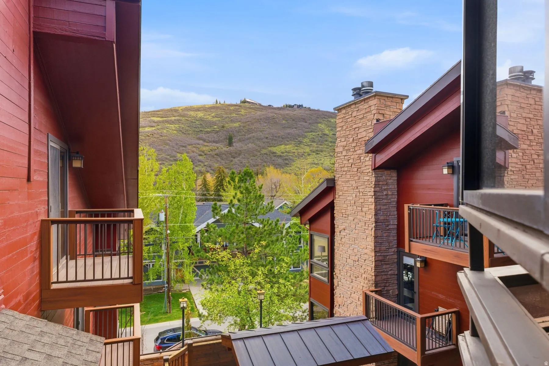 Exterior featuring balconies, red siding, stone chimneys, and a dark metal roof