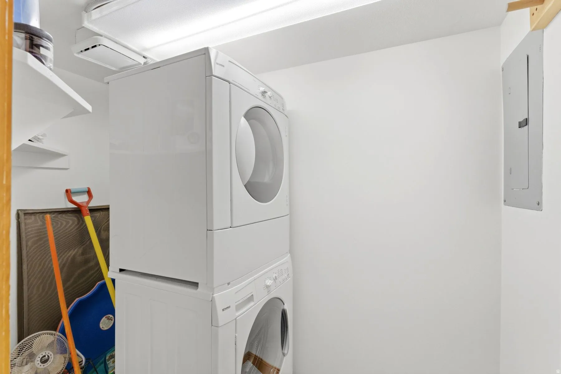 Dedicated laundry space featuring a stacked washer and dryer, ceiling-mounted lighting, and integrated wall shelving