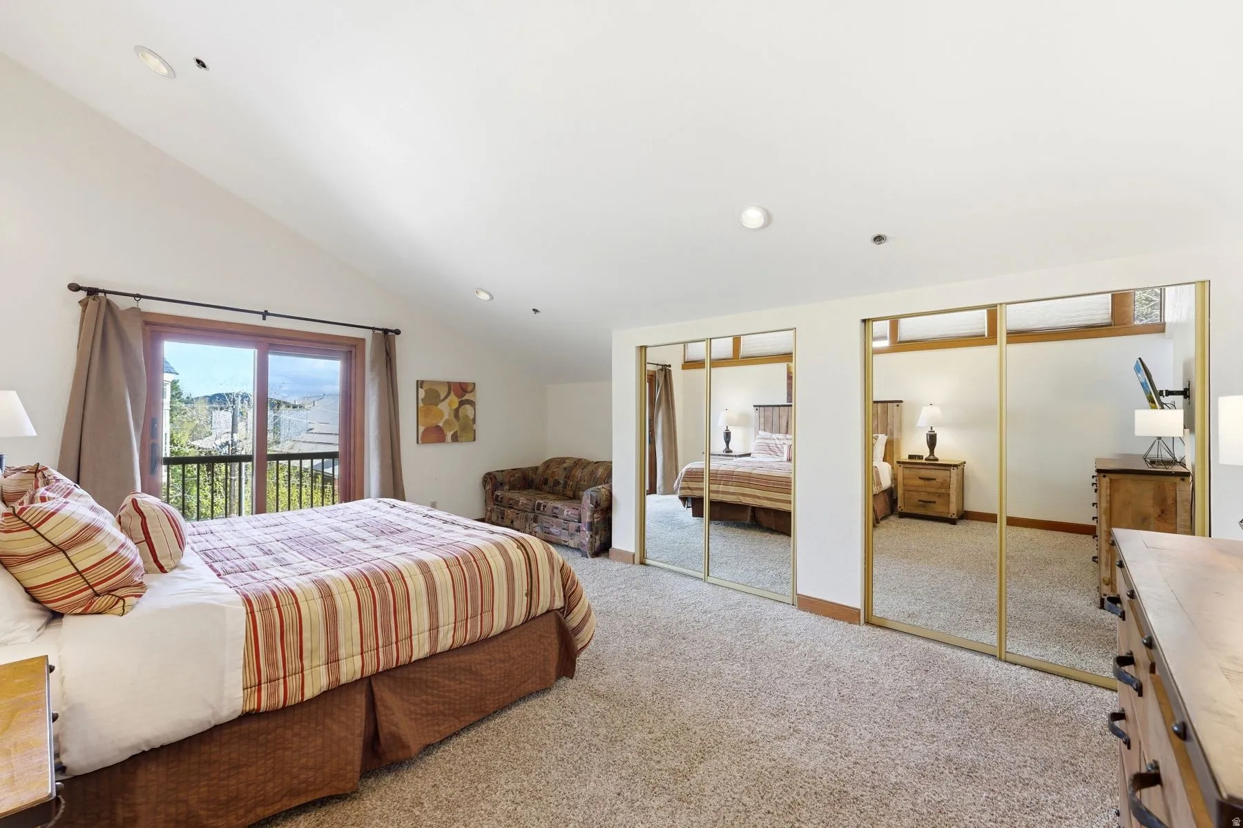 Sloped ceiling bedroom featuring a sliding glass door leading to an outdoor balcony with metal railings, recessed lighting, and mirrored closet doors