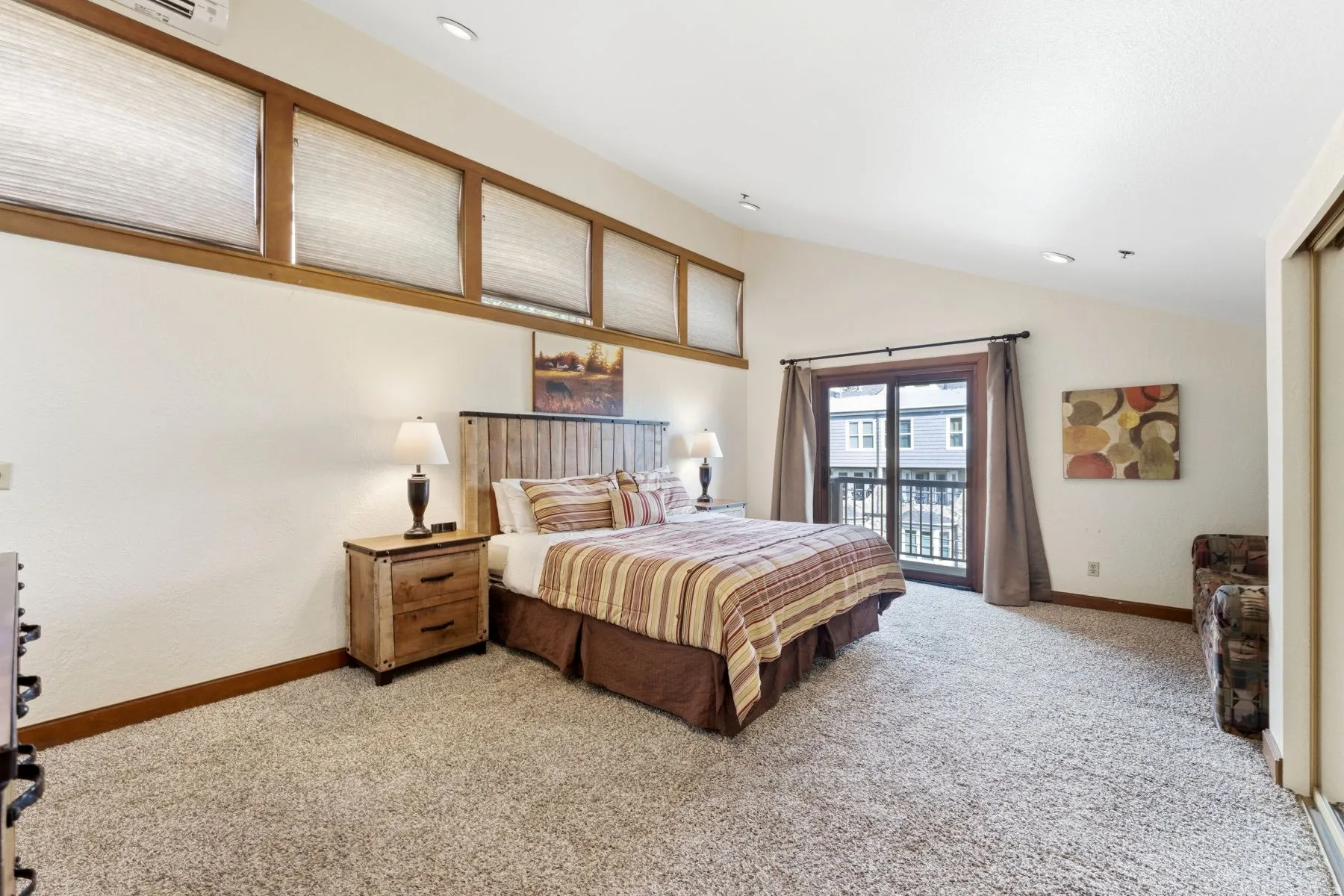 Spacious bedroom featuring vaulted ceilings, a private balcony with exterior railing, and a full-height glass sliding door