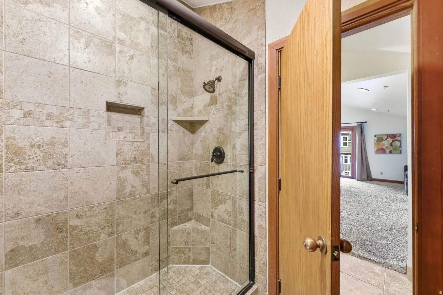Tiled shower enclosure featuring a glass door, built-in recessed shelf, and corner shelf