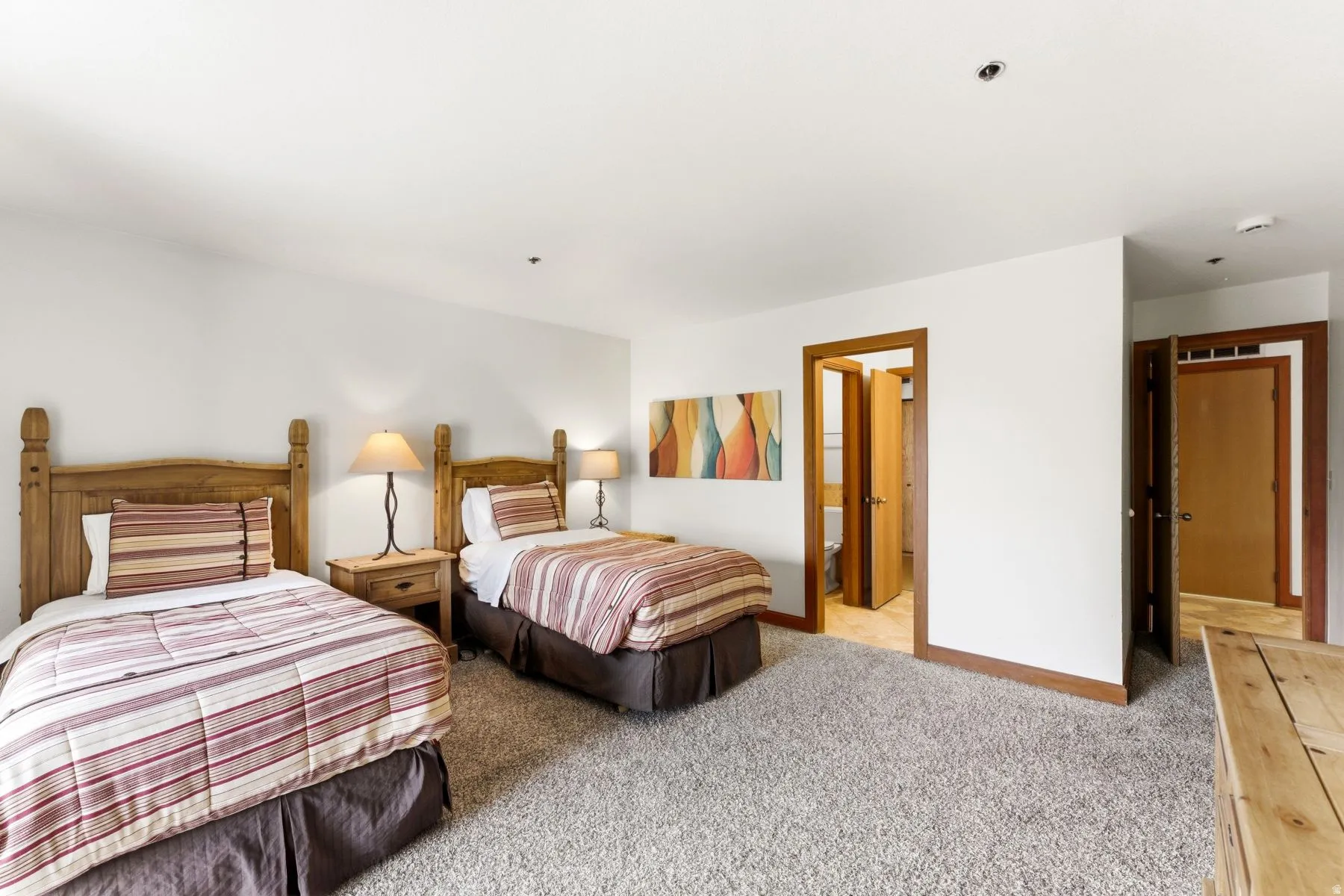 Carpeted room featuring two wood-frame beds, a wood-finish nightstand, white walls, and wood trim around doorways