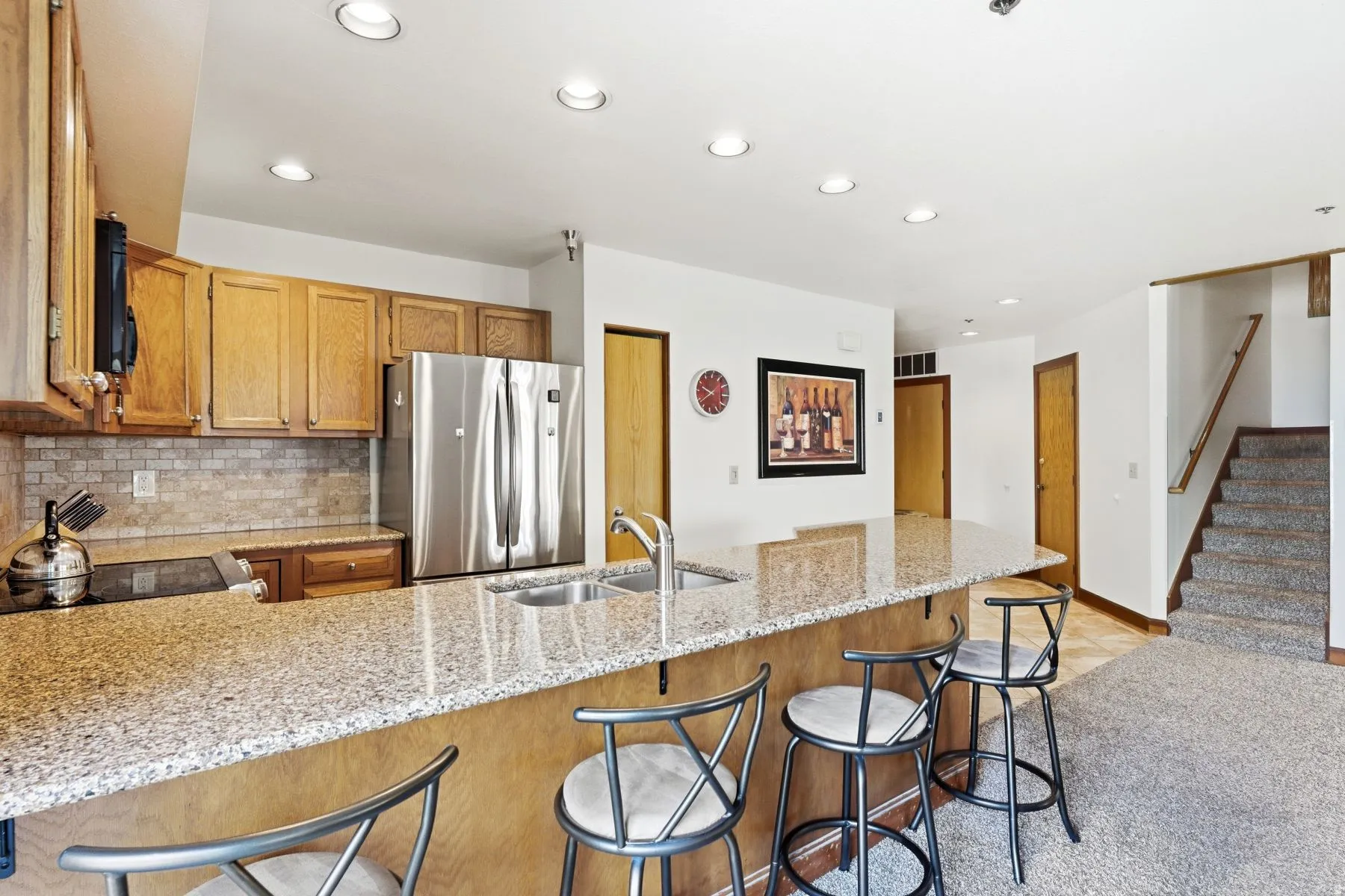 Kitchen featuring a large granite-style island with built-in stainless steel sink, wood-finish cabinetry, and stainless steel French door refrigerator