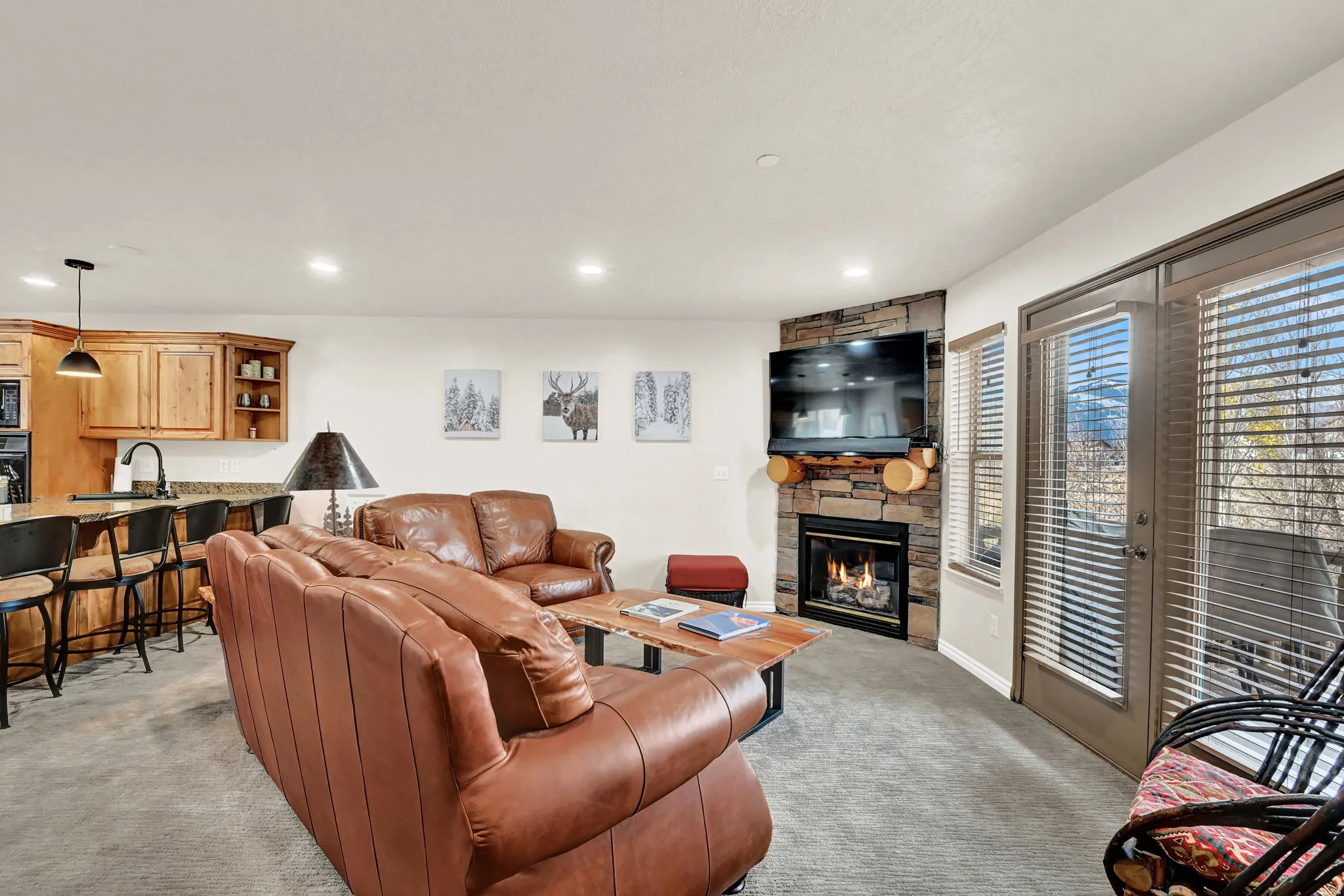 Living area featuring a stone-clad fireplace with built-in log storage, corner-mounted television, and direct outdoor access via glass doors