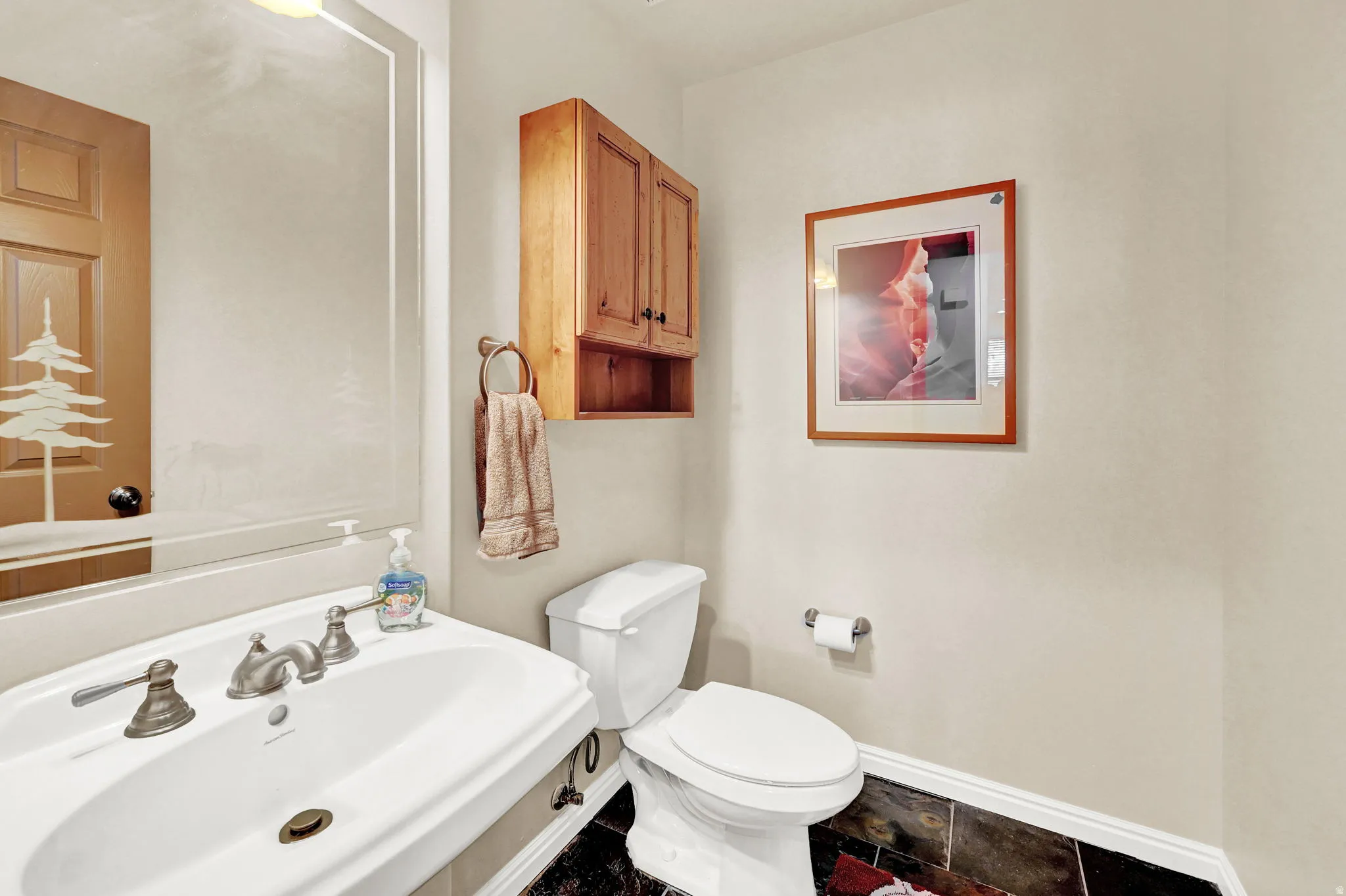 Pedestal sink with dual-handle faucet, framed mirror, and wood-finish cabinetry