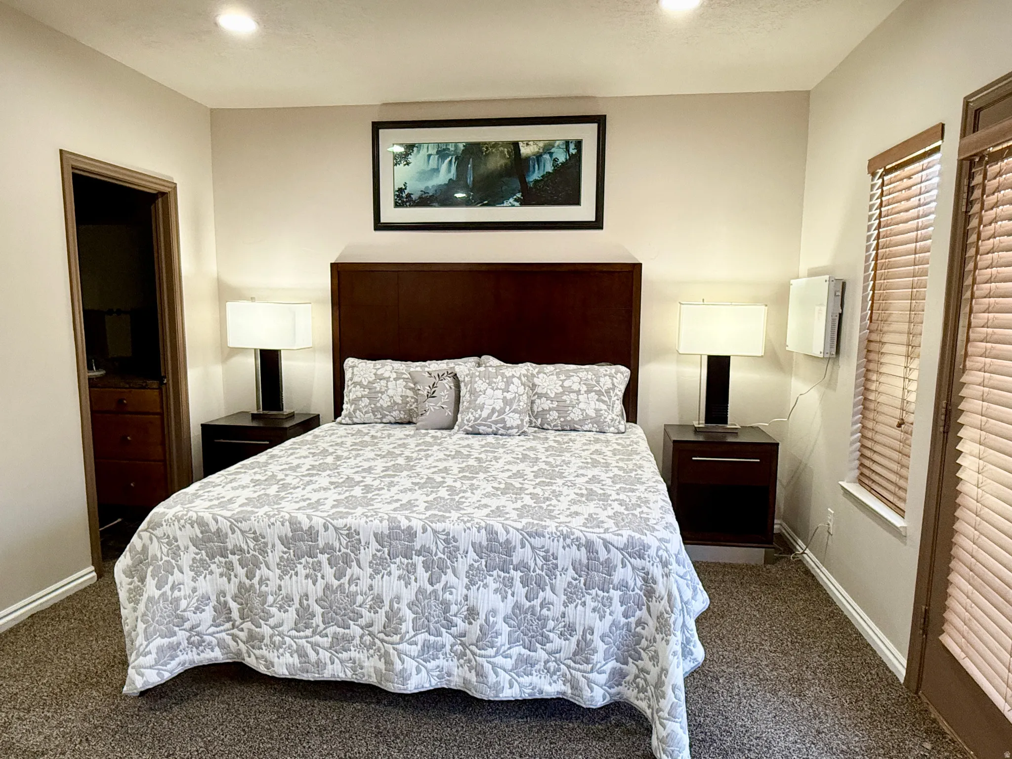 Spacious sleeping area featuring a dark wood headboard, recessed lighting, and textural carpet flooring