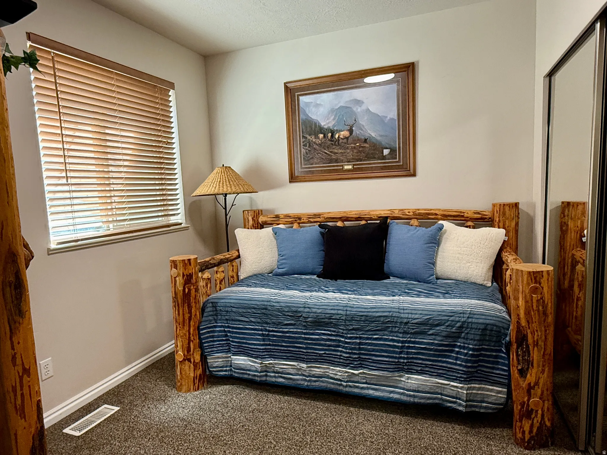 Carpeted interior space featuring a window with wooden blinds, a mirrored closet door, and light-toned wall paint