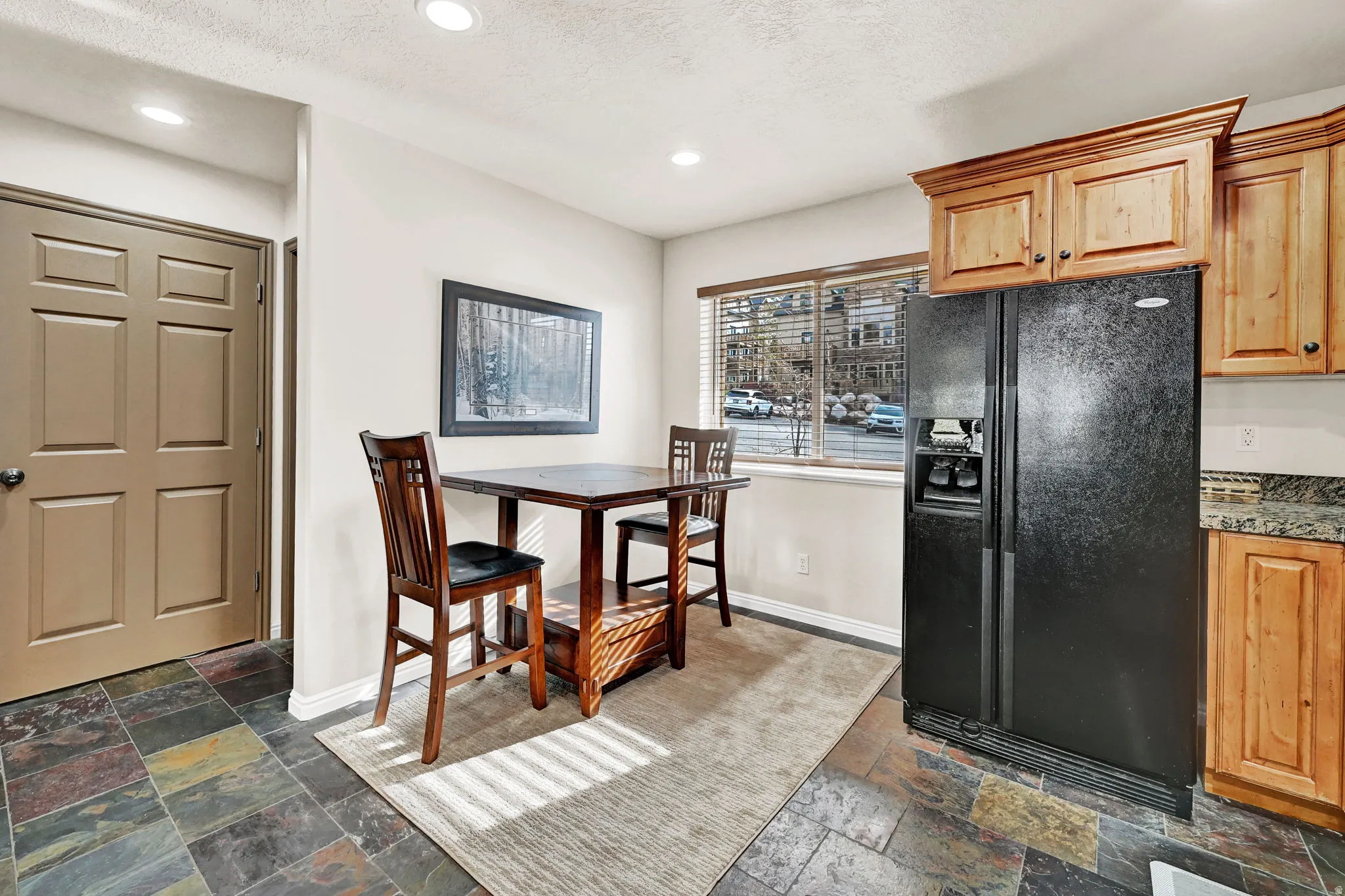 Kitchen area featuring natural wood cabinetry, a black side-by-side refrigerator, and a window with blinds