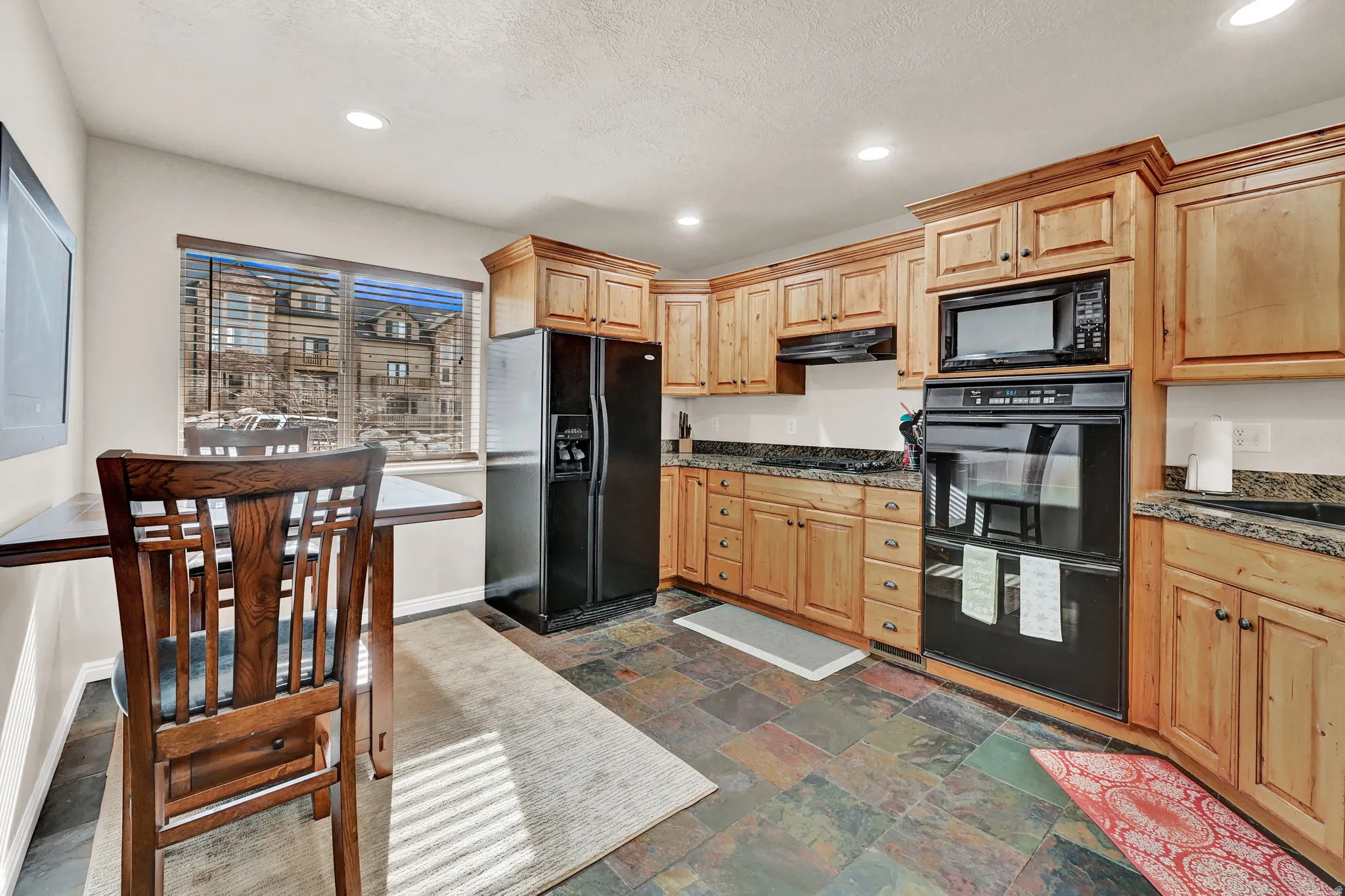 Kitchen featuring wood-finish cabinetry, black appliances, stone-look countertops, and slate flooring