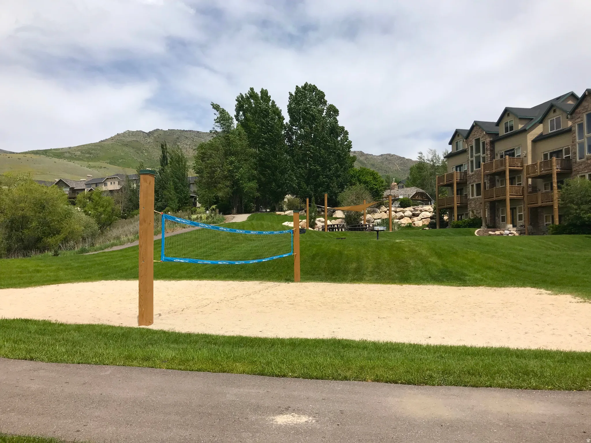 Sand volleyball court with a blue net, surrounded by green lawns