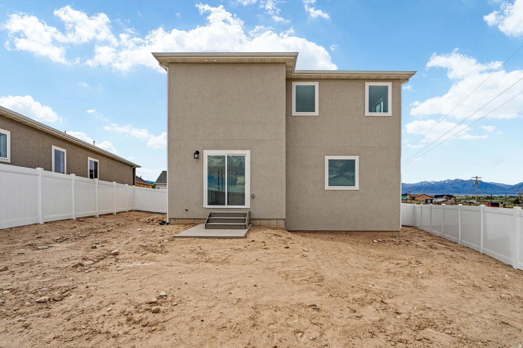 Rear exterior featuring stucco siding, multiple windows, a sliding glass door, a concrete patio, and a white privacy fence enclosing the property