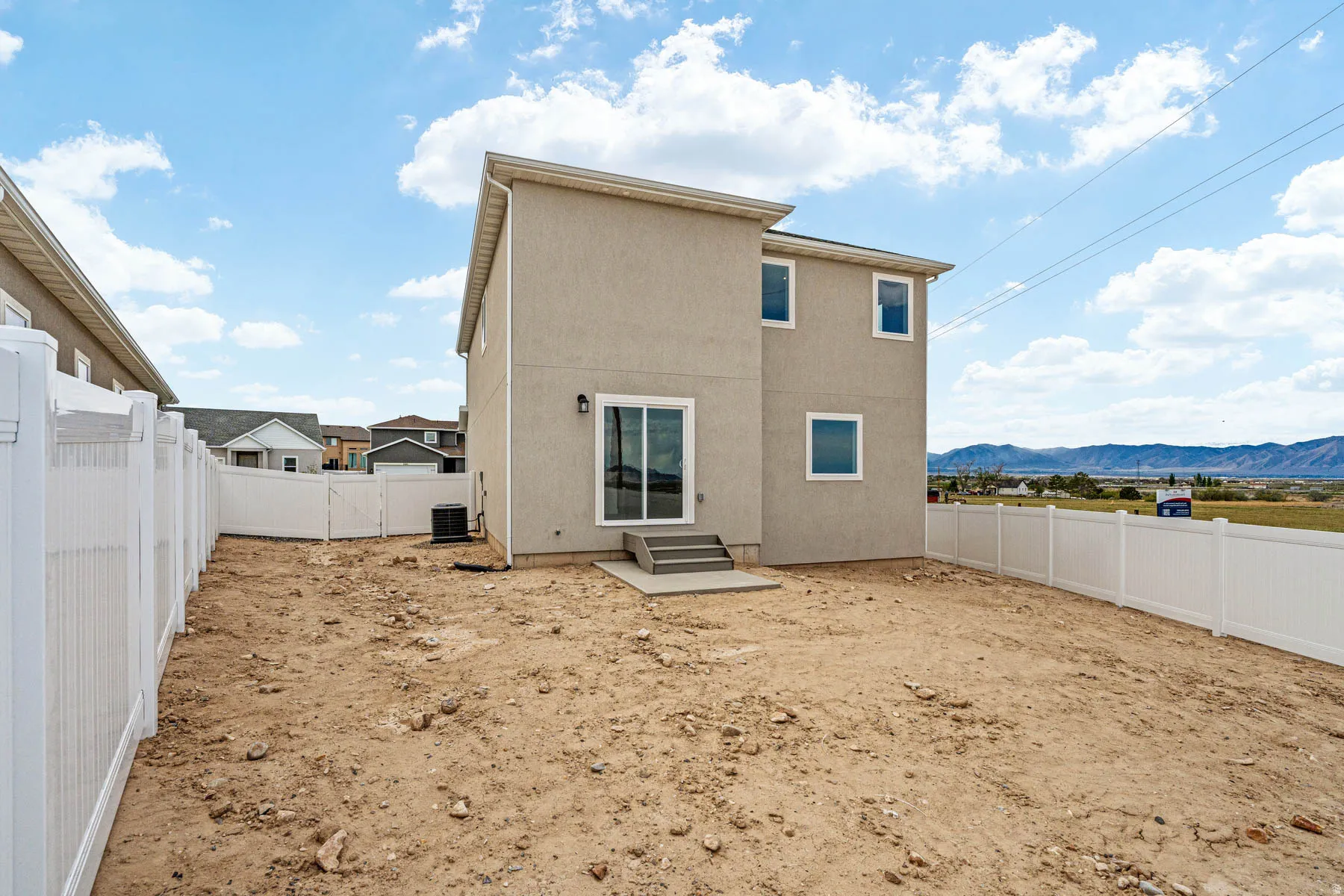 Rear exterior featuring a two-story stucco facade, multiple windows, and a sliding glass door with concrete steps