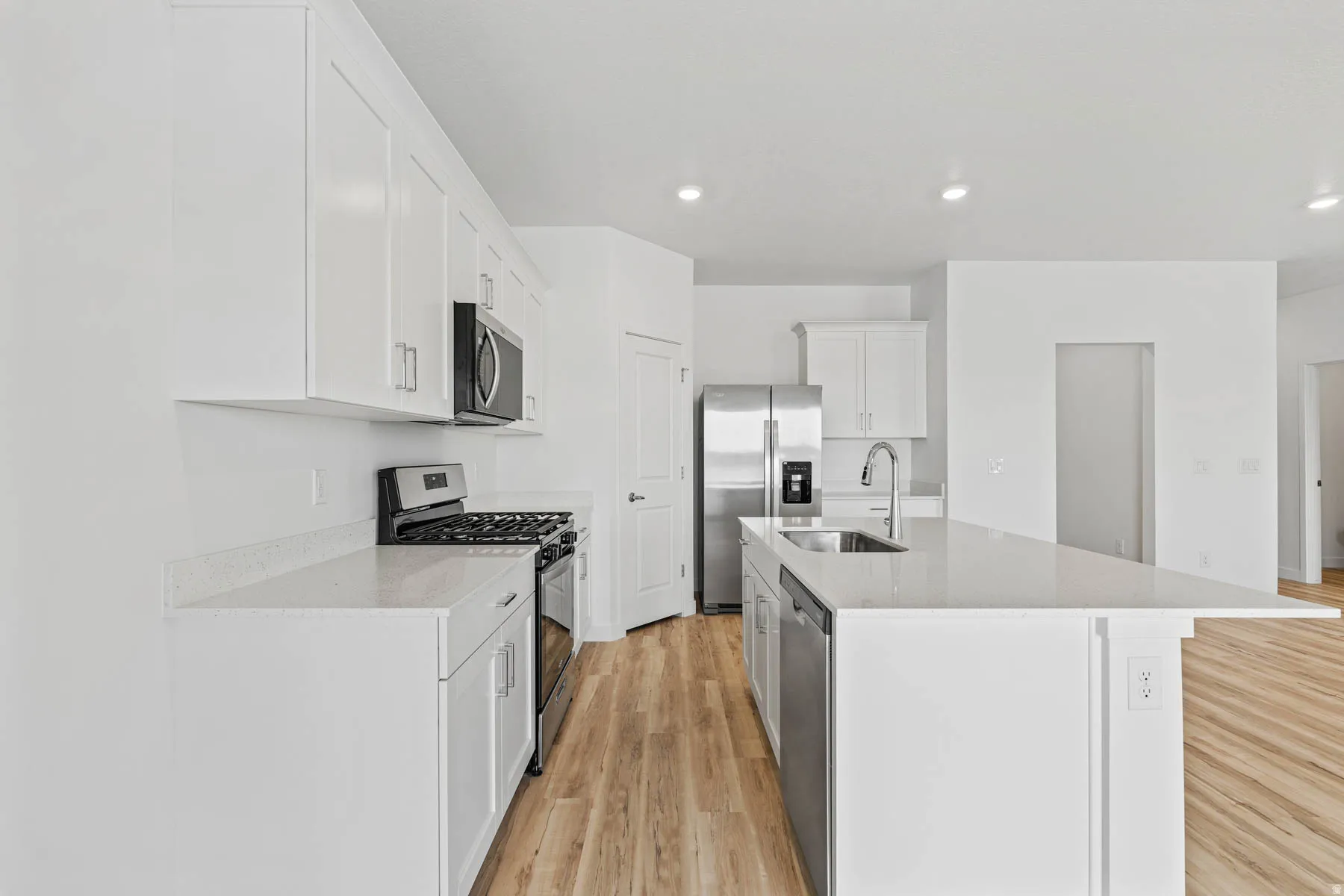 Modern kitchen featuring white cabinetry, light-toned countertops, stainless steel appliances, and wood-finish flooring