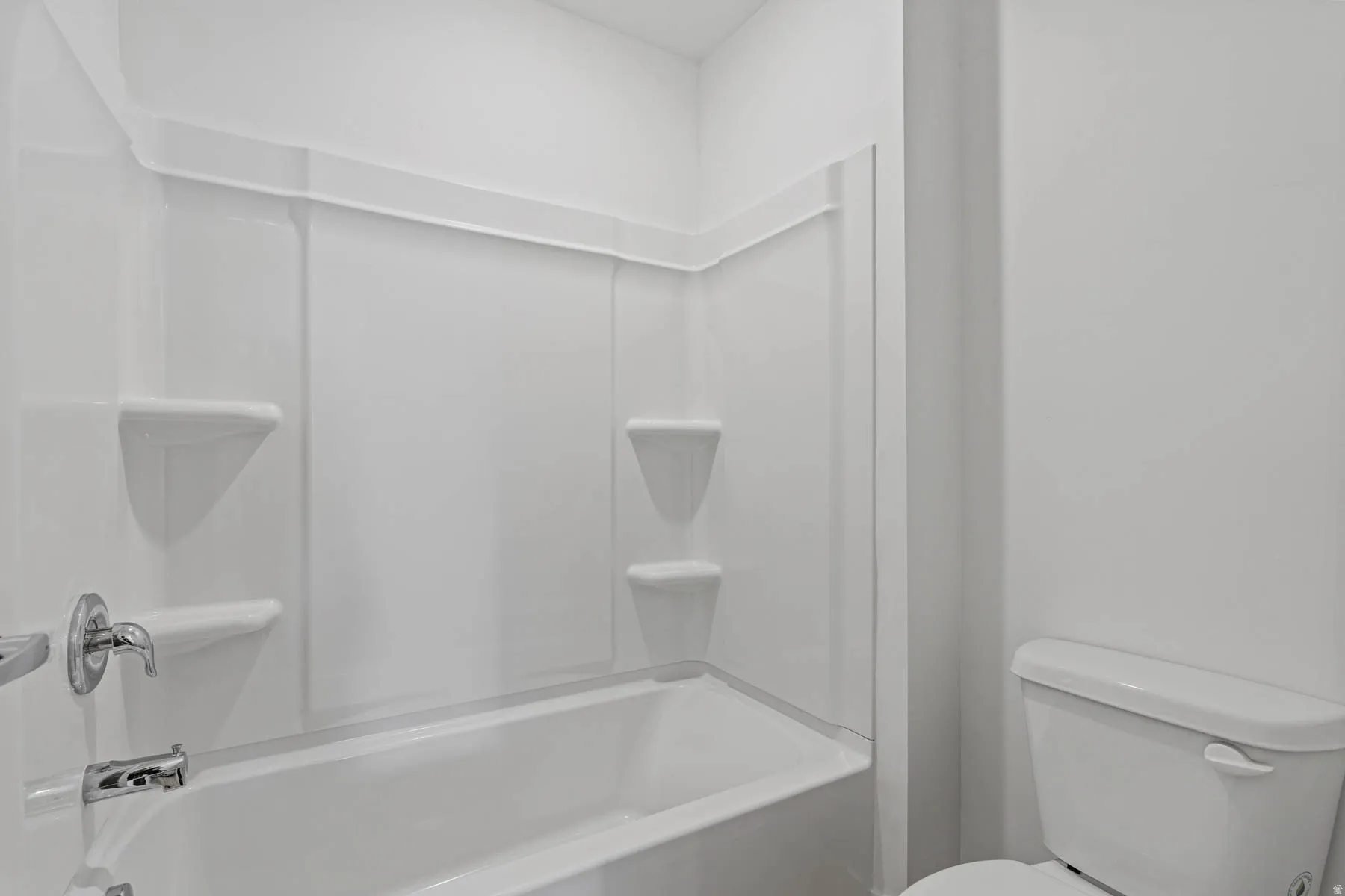 White bathtub and shower surround with integrated shelving, accompanied by a white toilet