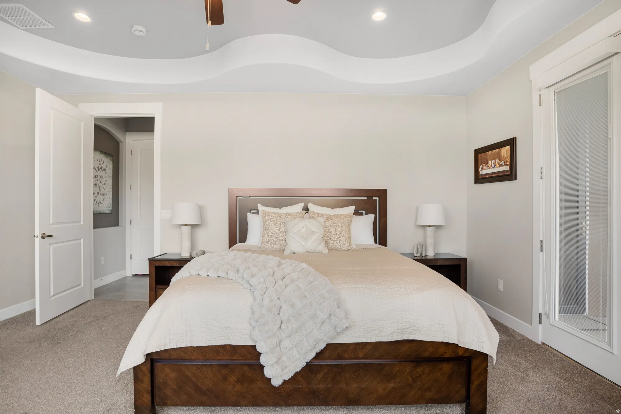 Carpeted bedroom featuring a decorative tray ceiling with recessed lighting and a ceiling fan