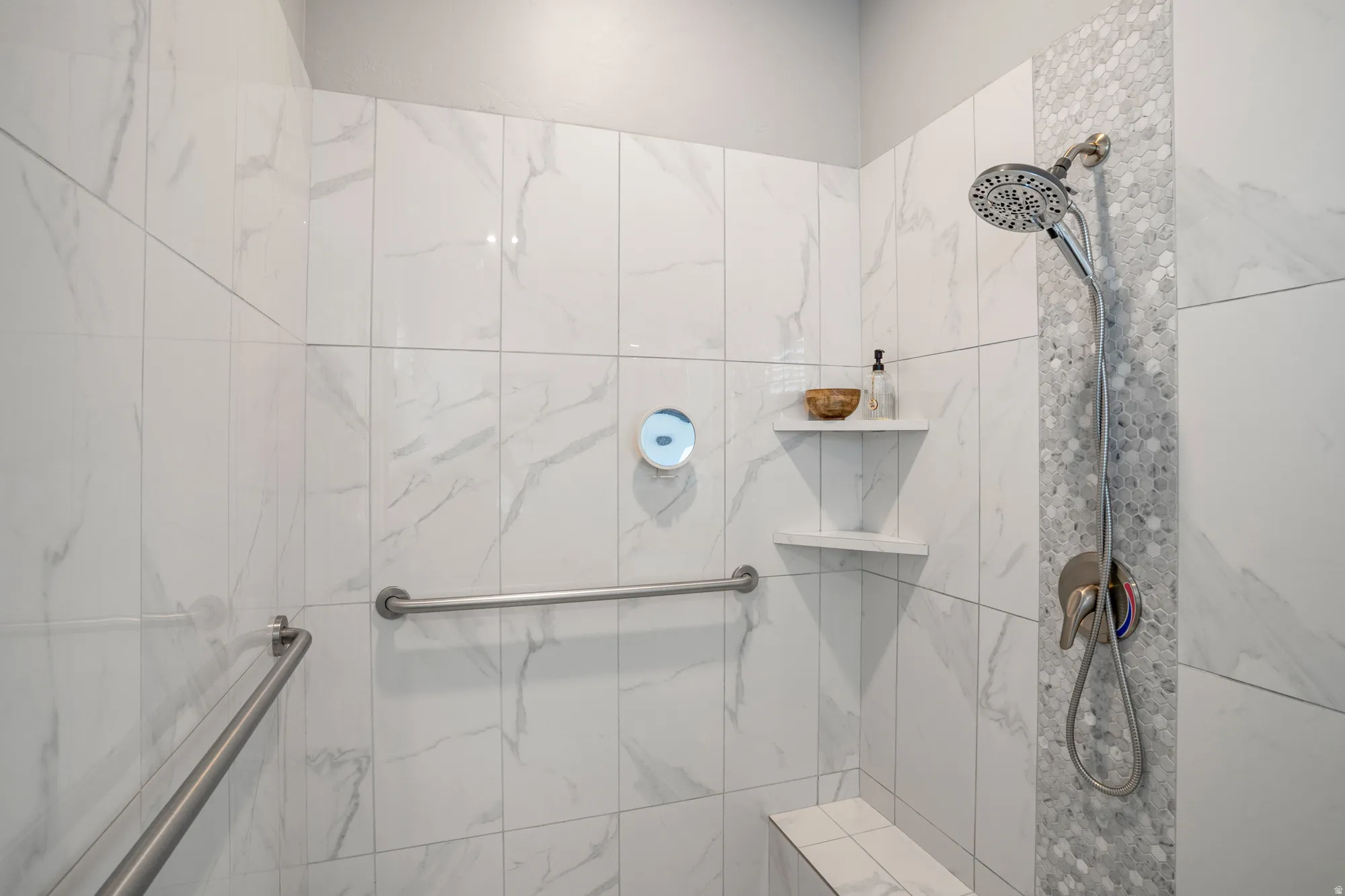 Shower stall featuring large format white tile with grey veining, a rainfall showerhead, and a mosaic tile accent strip