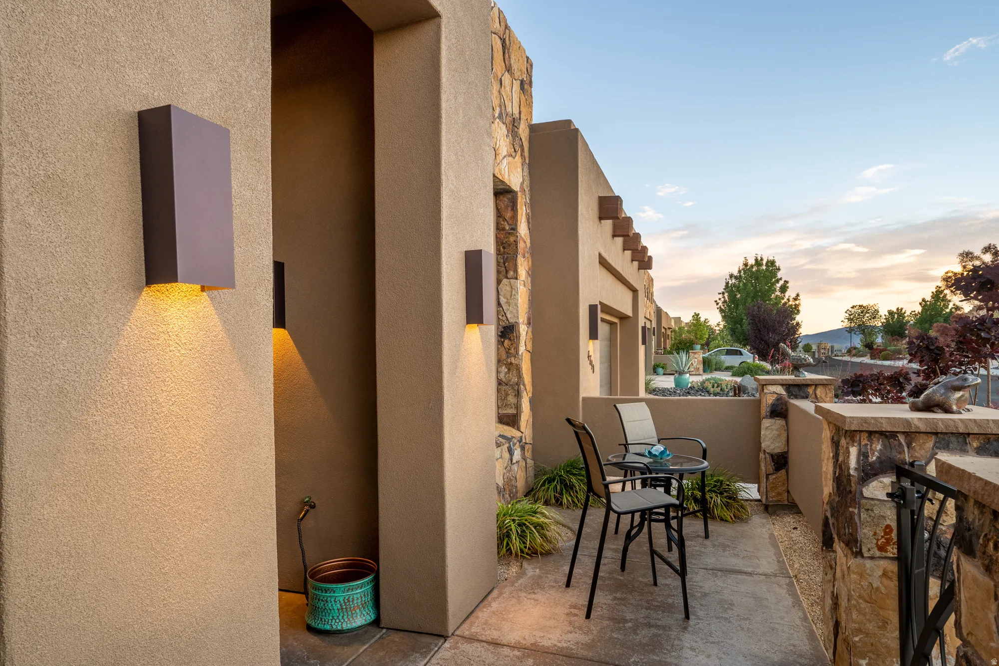 Exterior stucco walls featuring integrated sconce lighting, stone veneer accents, and a concrete patio