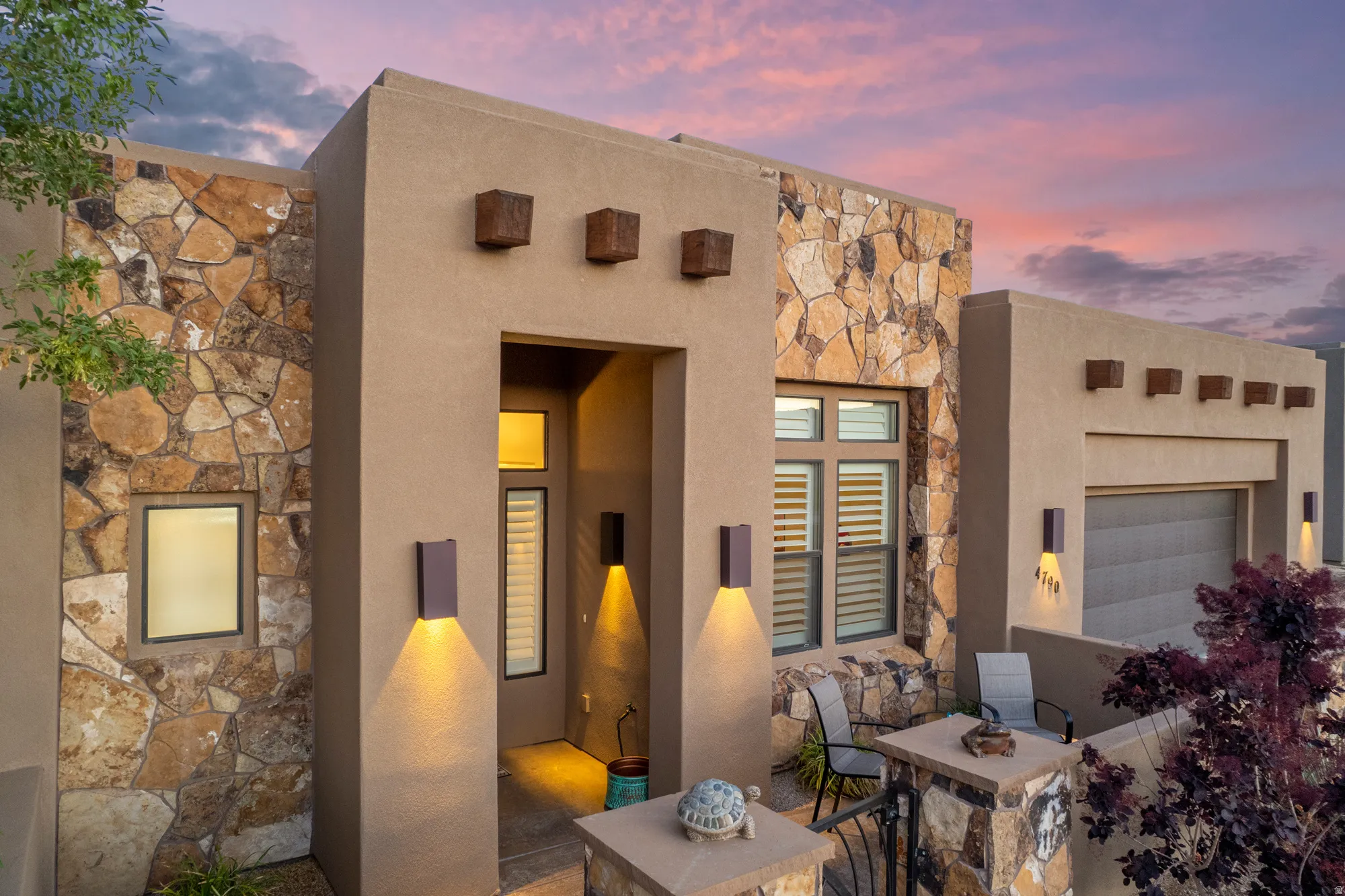 Stucco exterior with extensive stone accents, a deep recessed entry, modern exterior lighting, and a front patio area