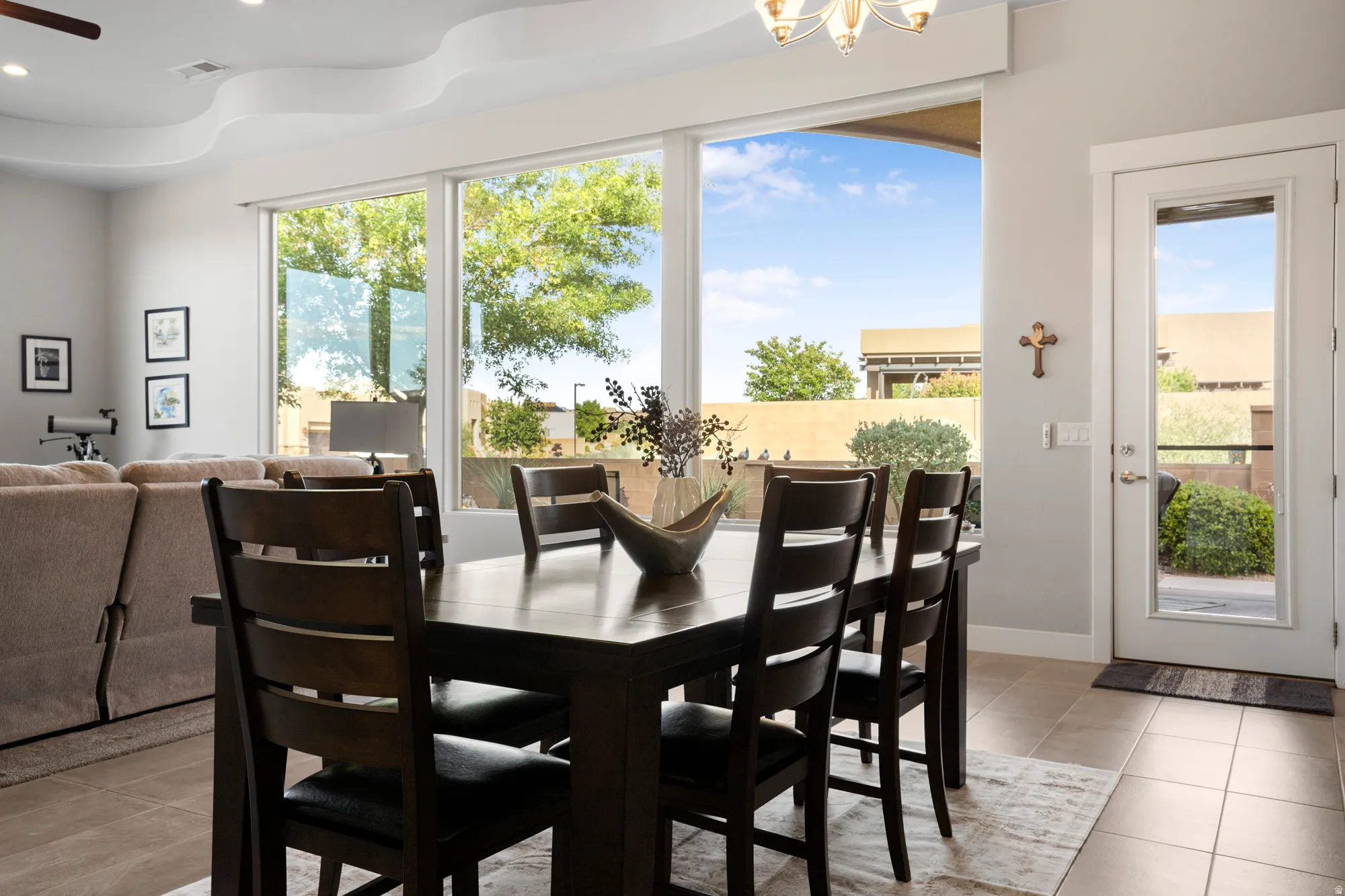 Dining area featuring a dark wood-finish table and chairs, large windows, a glass-panel exterior door, tray ceiling detail, and tiled flooring