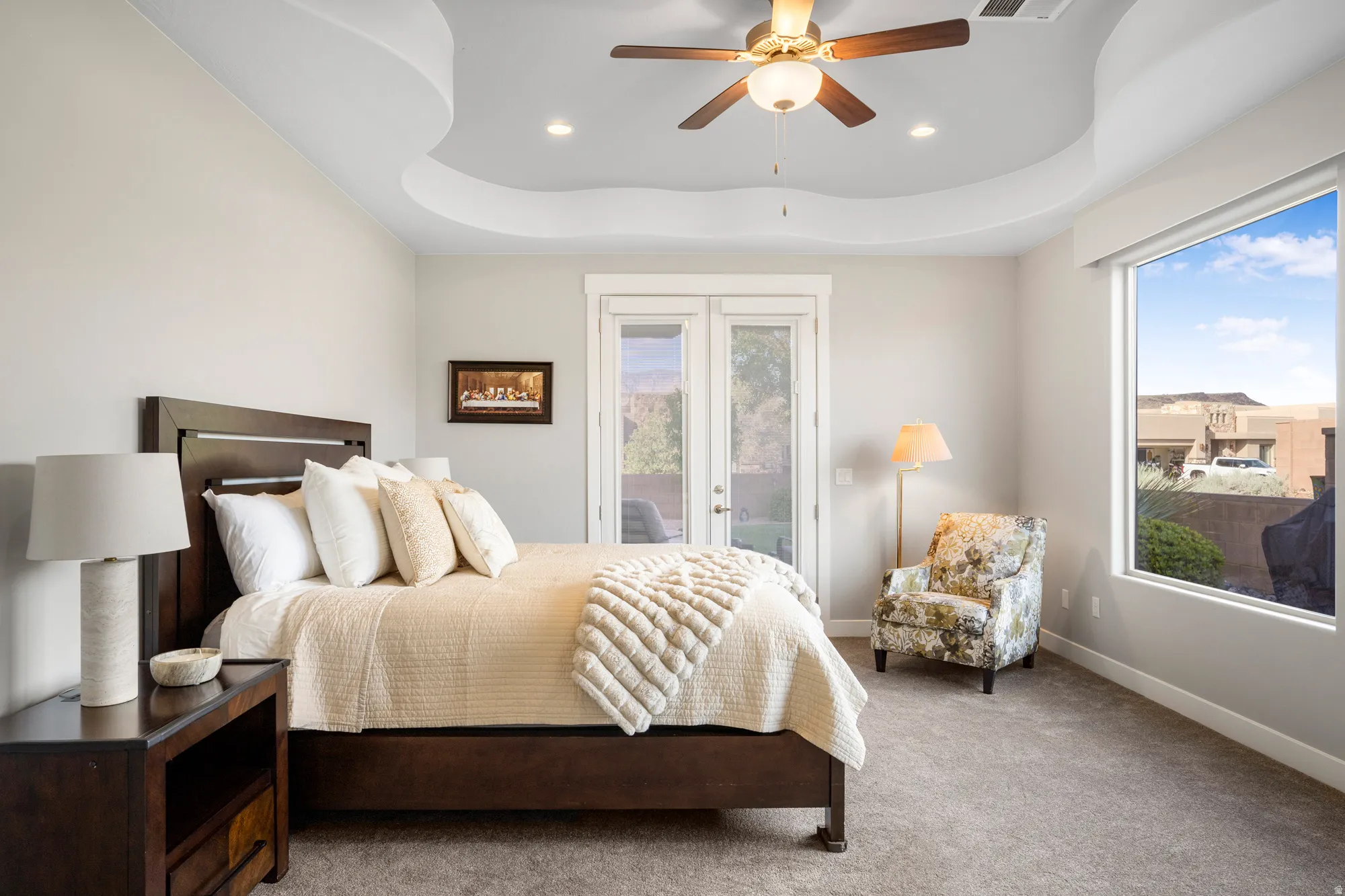 Tray ceiling with recessed lighting and a ceiling fan, accompanied by a large picture window and glass French doors