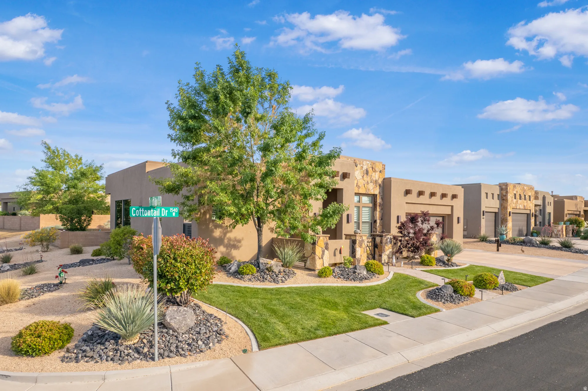 Exterior featuring stucco finishes, stone accents, mature trees, and landscaping with a mix of lawn and arid plantings