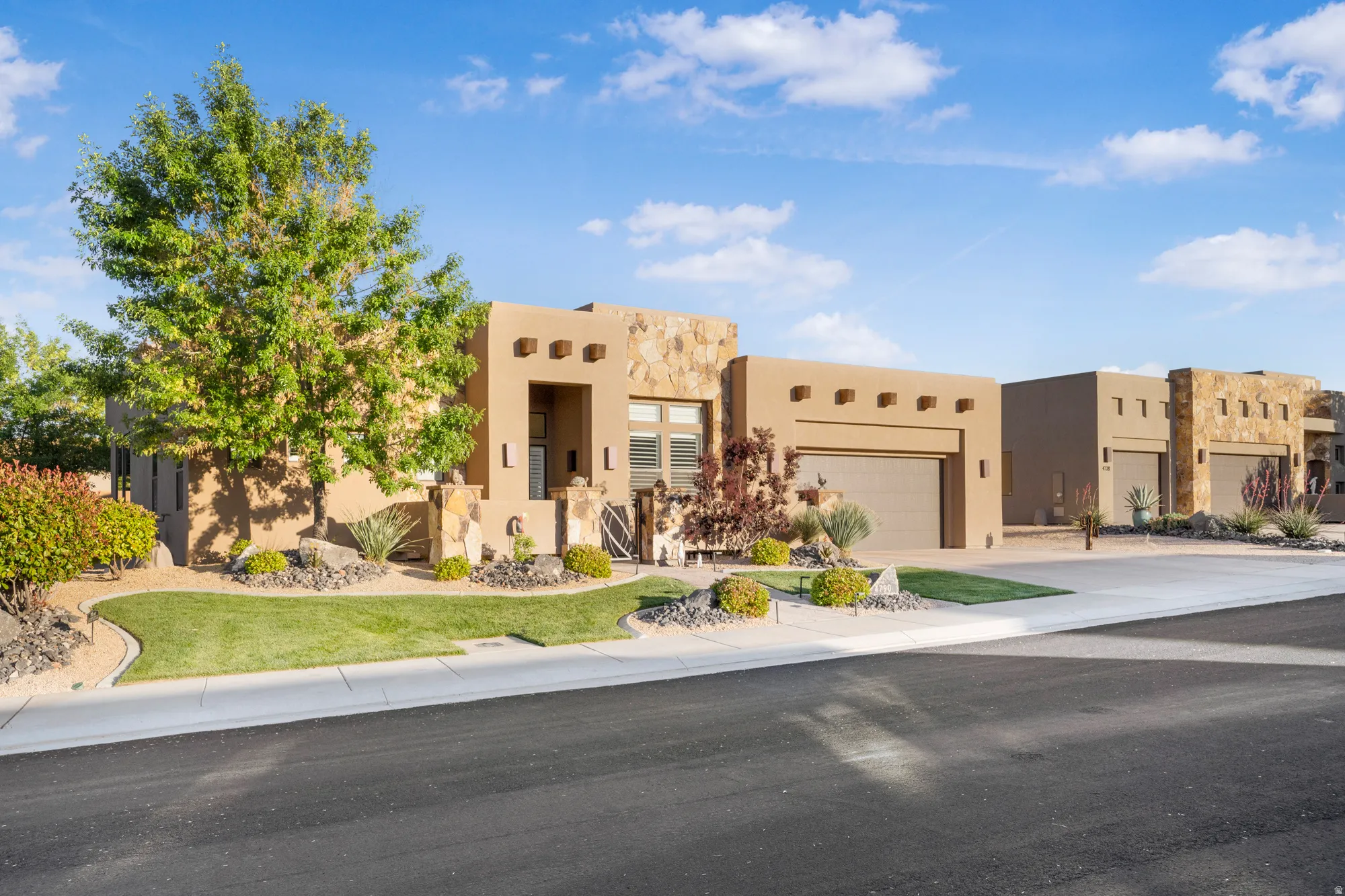 Contemporary stucco exterior featuring stone accents, an attached garage, and manicured landscaping
