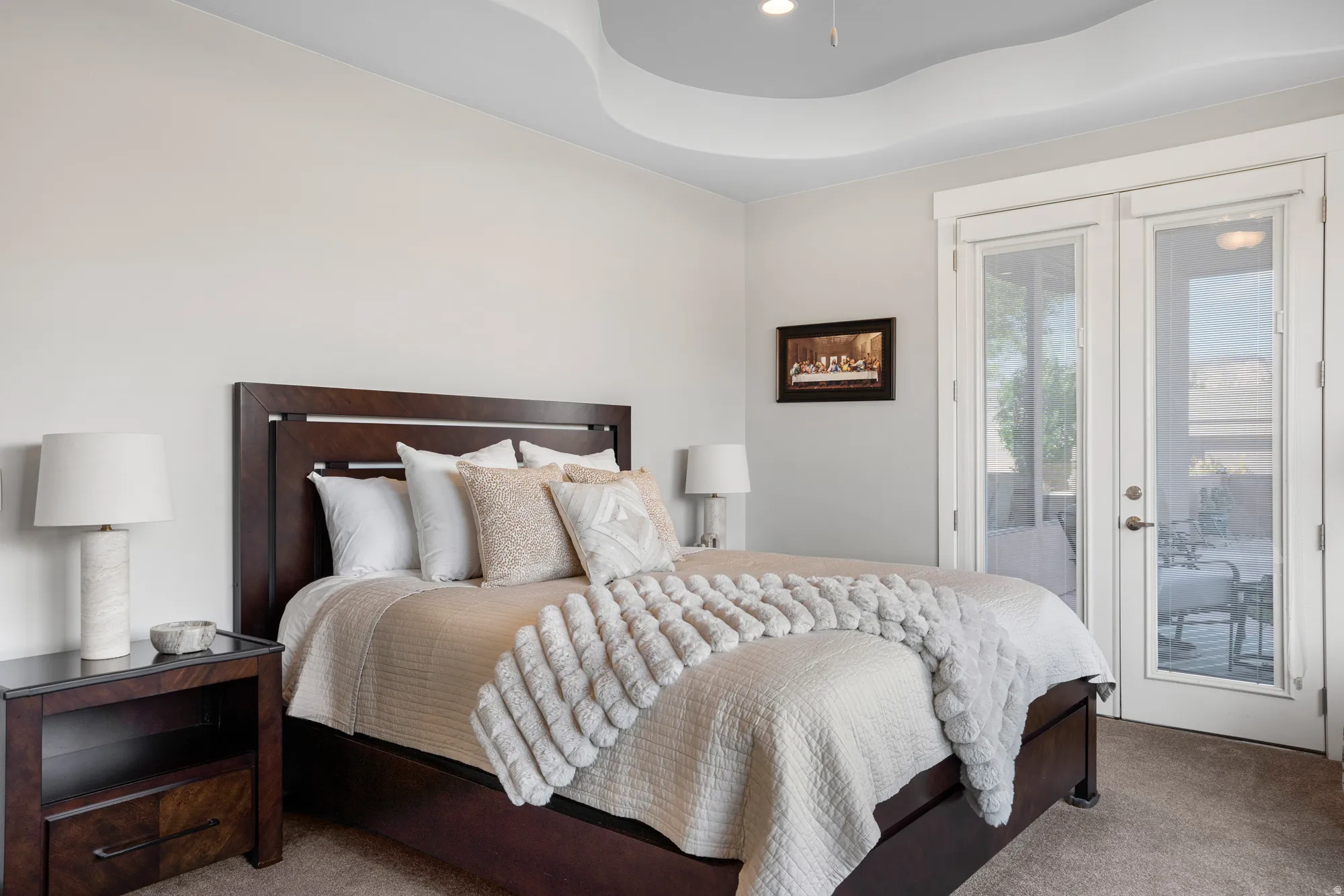 Spacious bedroom featuring an elegant tray ceiling, glass-paneled French doors providing direct outdoor access, and plush carpet flooring