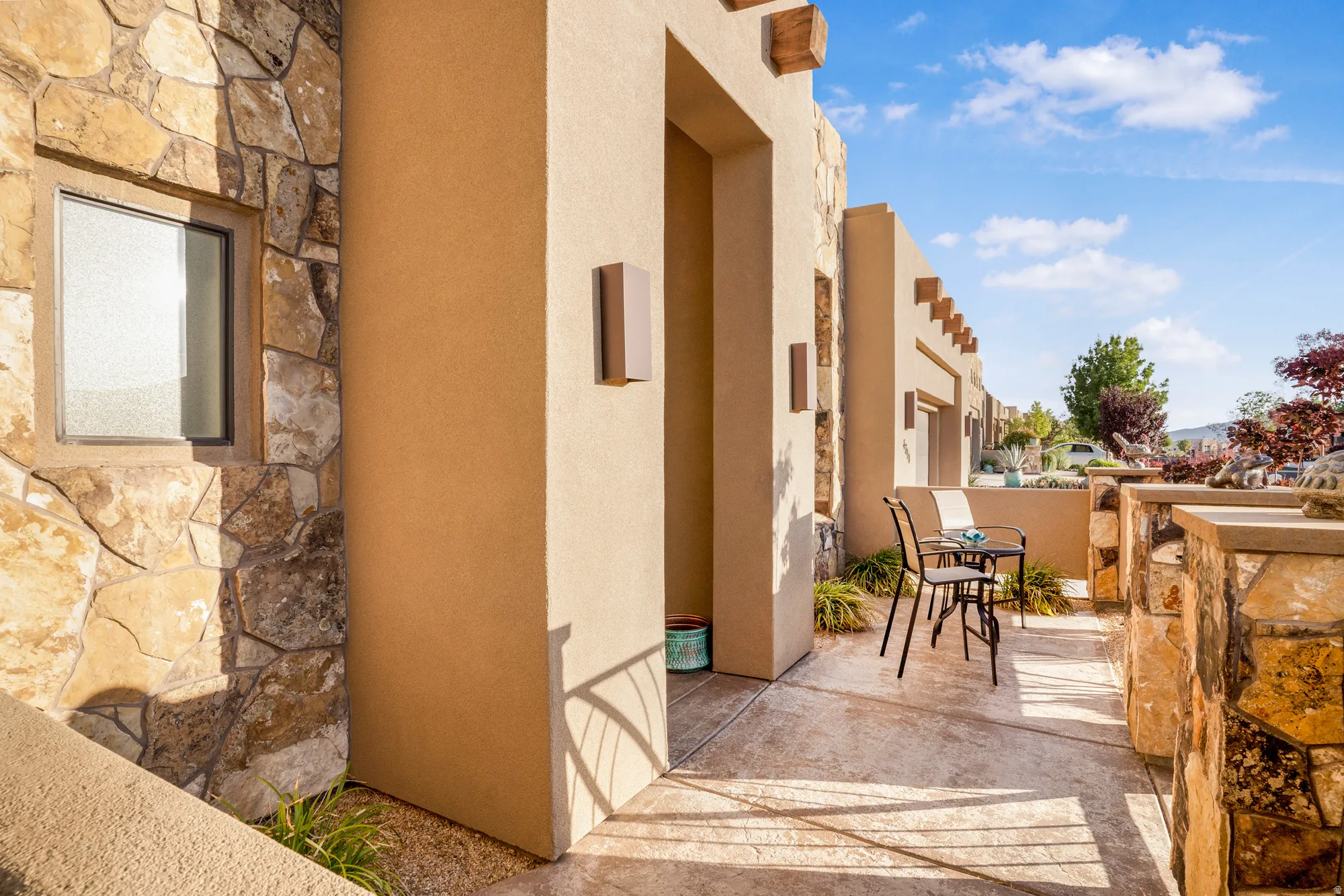 Outdoor patio featuring a textured concrete surface, stone veneer walls, stucco exterior, and decorative wood beams