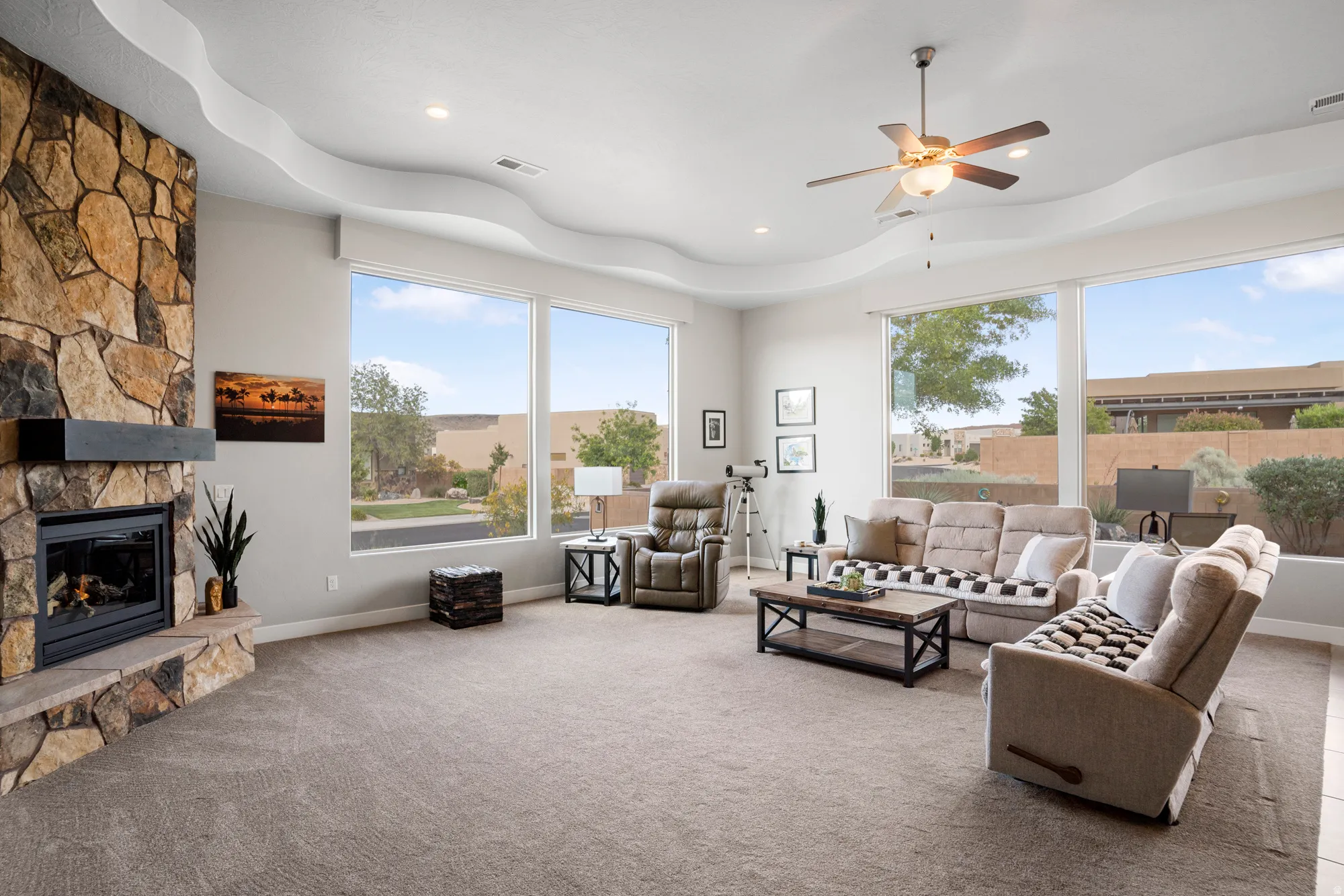 Spacious living area featuring a stone-clad fireplace with a dark wood mantle, wall-to-wall carpeting, and a ceiling fan