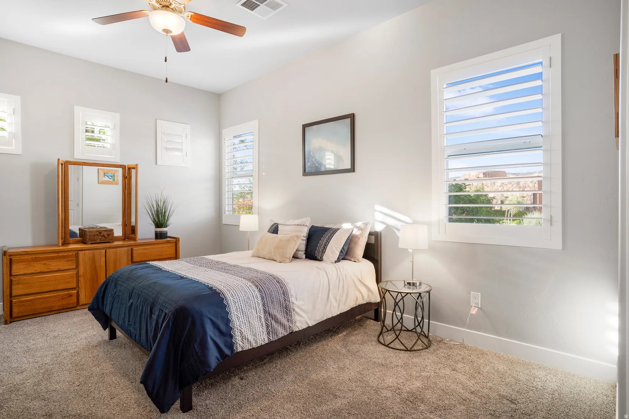 Carpeted interior space featuring multiple windows with white plantation shutters, a ceiling fan with integrated lighting, and light-toned wall finishes