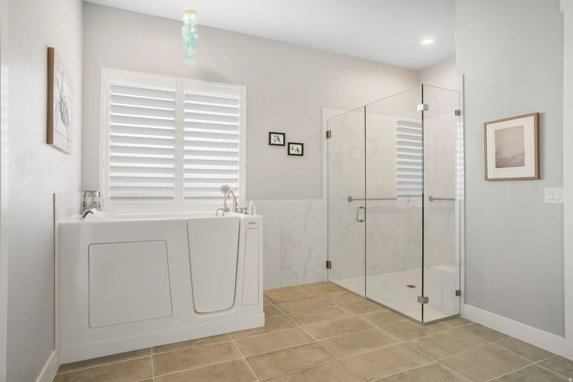 Spacious bathroom featuring a walk-in tub with a window, a glass-enclosed shower with white tiled walls, and large format floor tiles