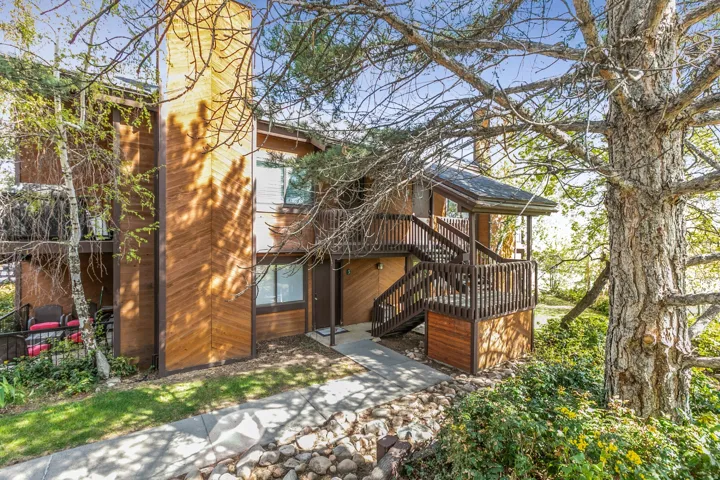Multi-level property featuring wood-paneled exterior siding, a covered entry porch, and an exterior staircase with dark wood railings