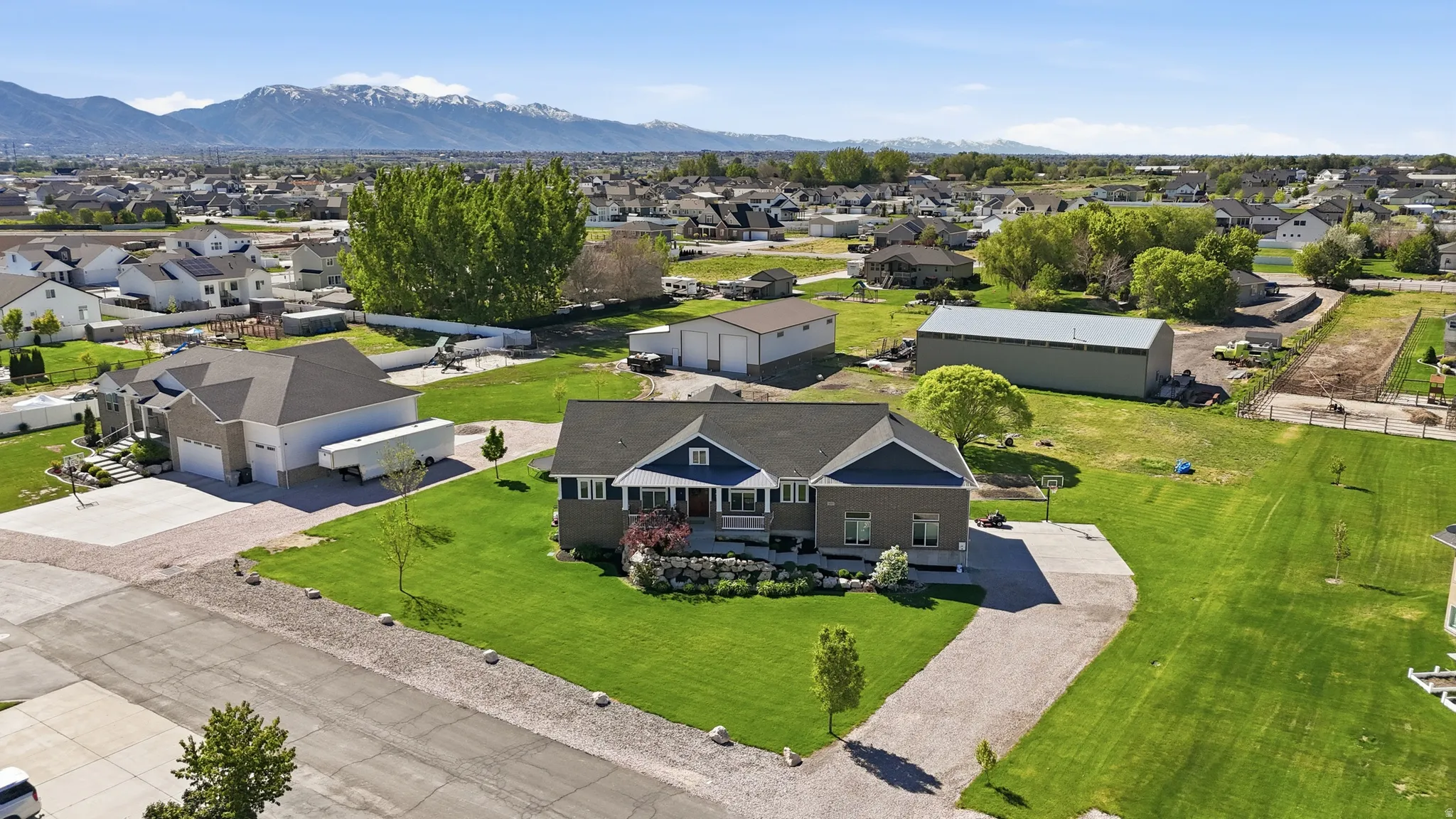 Expansive property featuring a meticulously maintained lawn, a gravel driveway, and a two-story home with a blue siding and stone exterior
