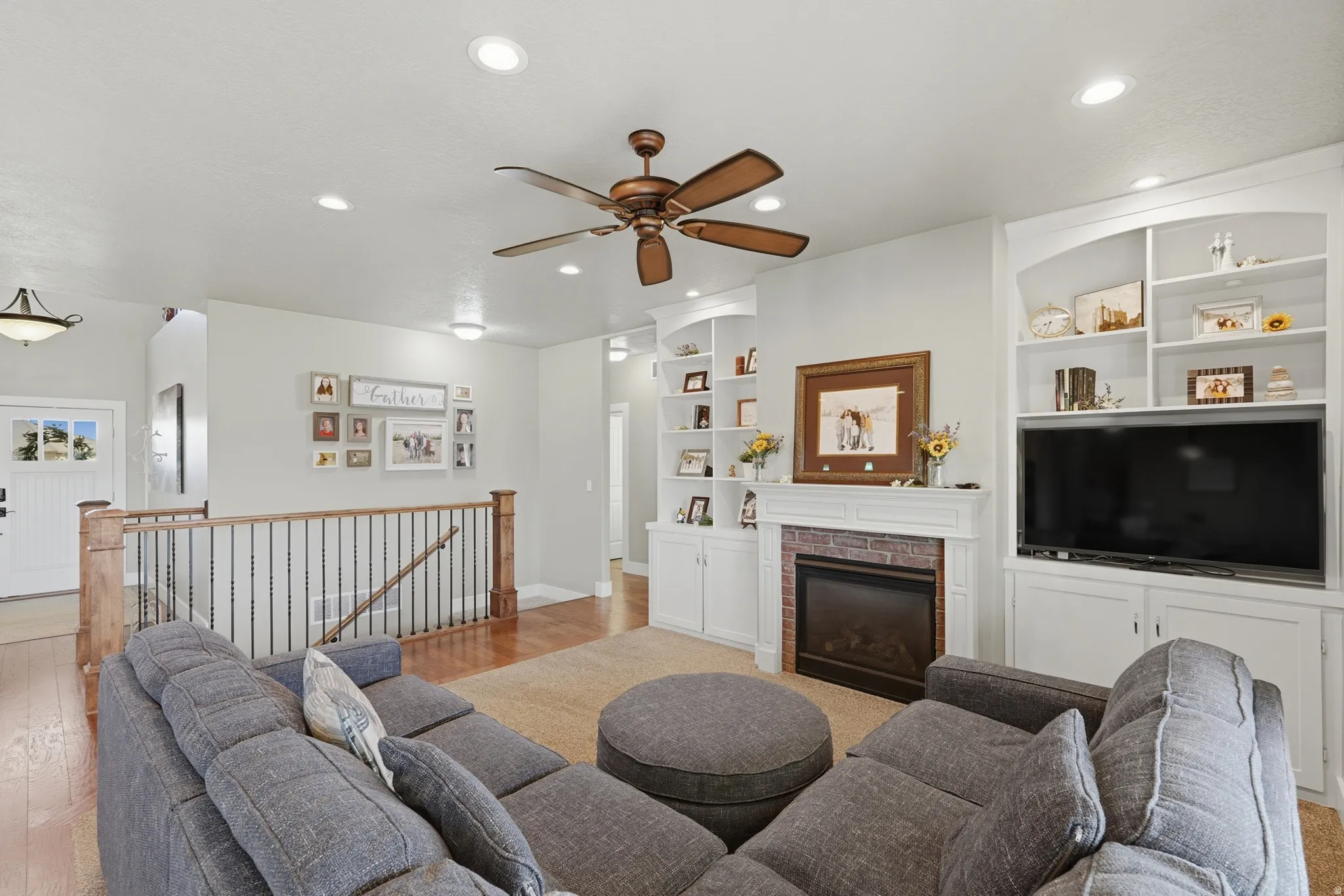 Living area featuring a central fireplace with brick surround and white mantel, flanked by built-in white cabinetry and shelving